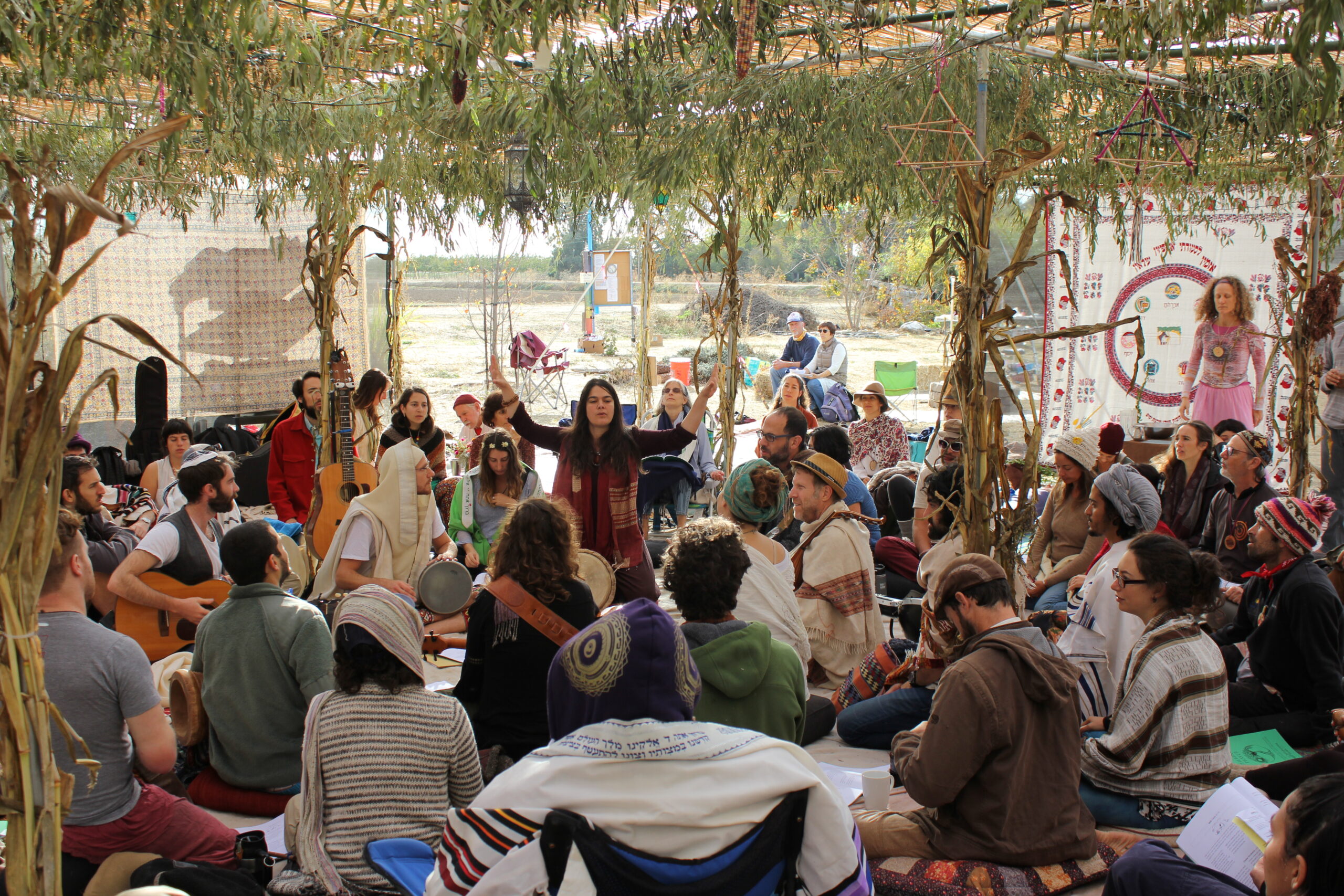 under a very large sukkah, shere raises her hands up as she leads a circle of people in prayer