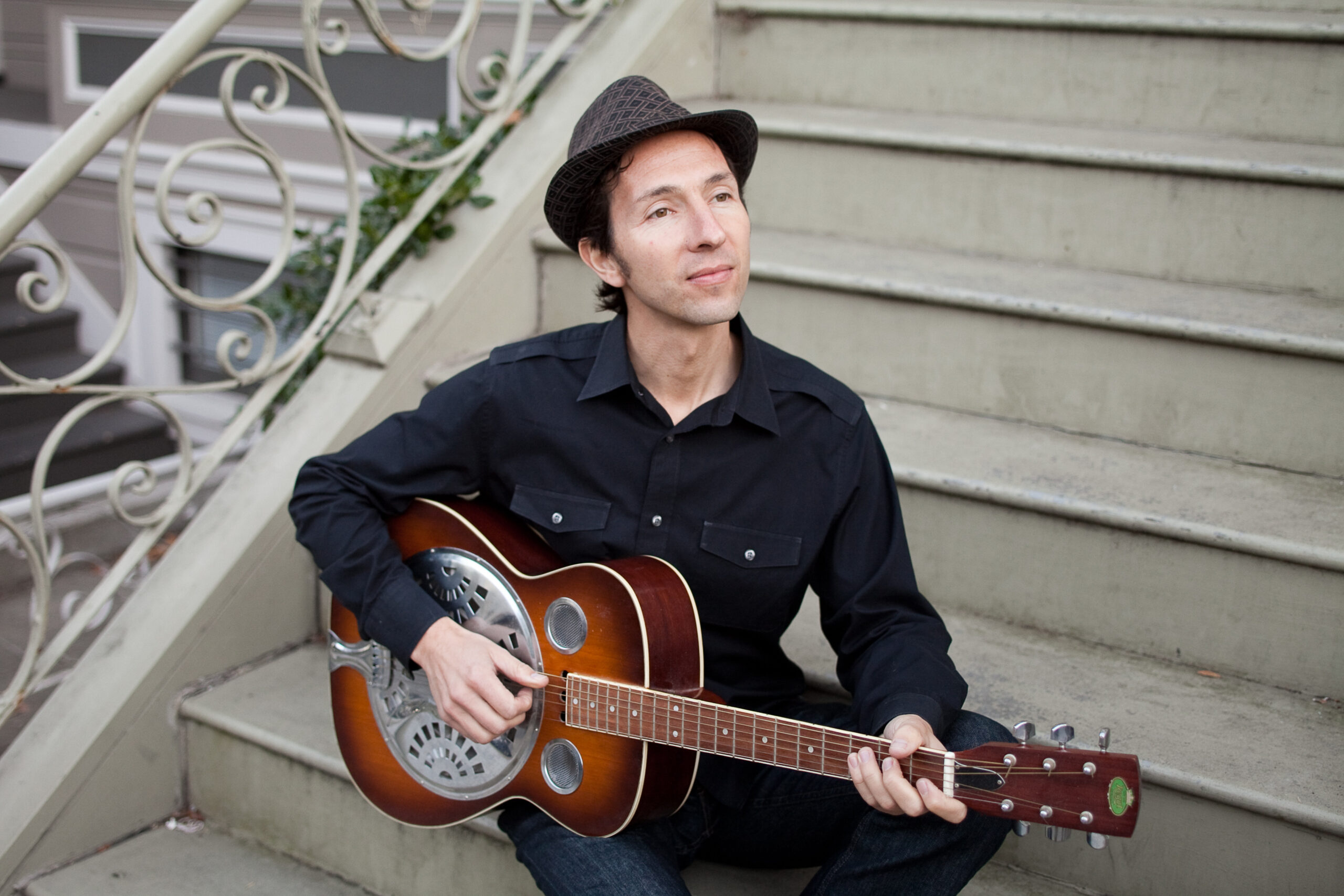 Saul Kaye sitting a stoop with a steel guitar