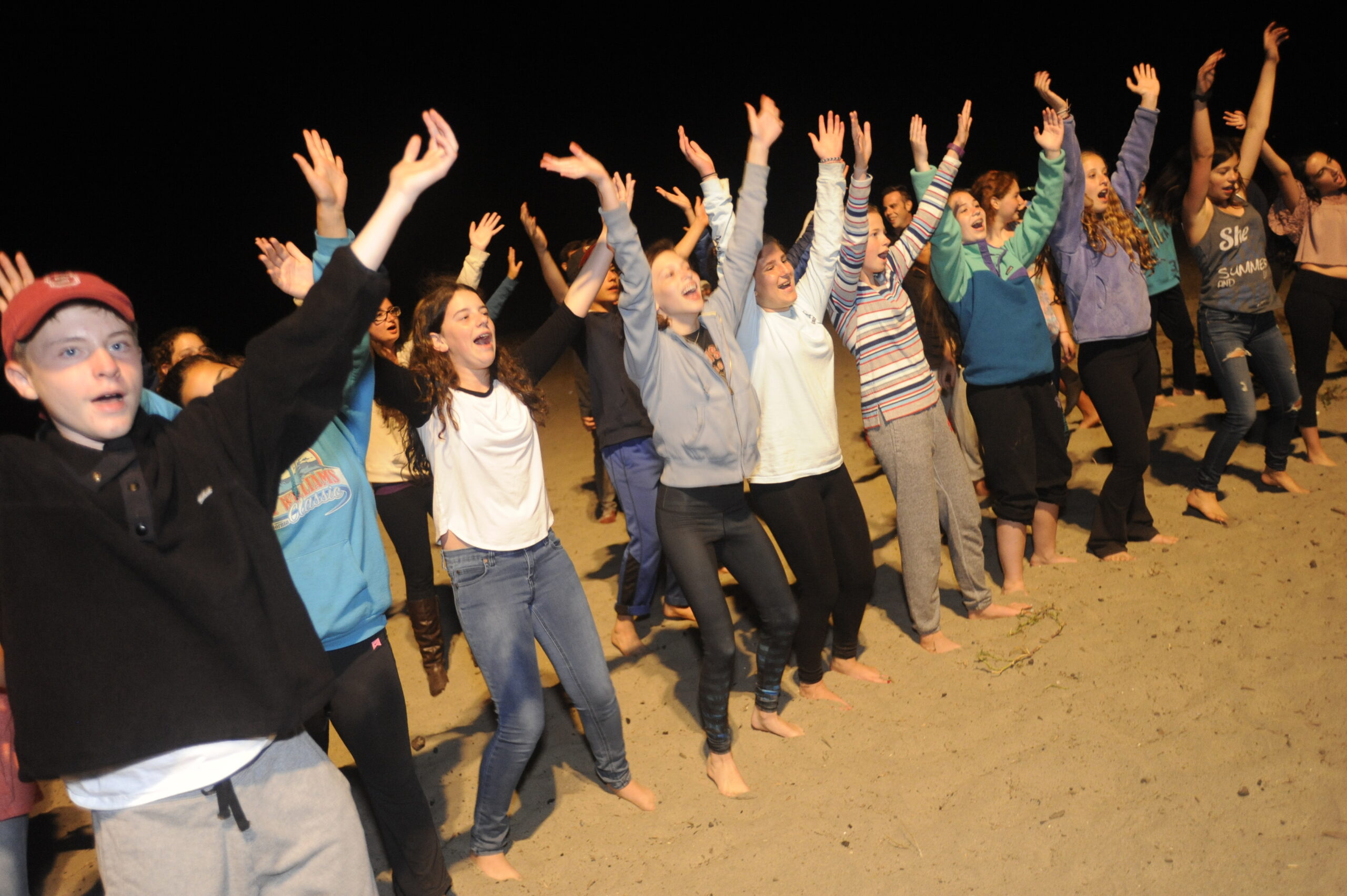 children lined up on the beach at night waving their arms in the air