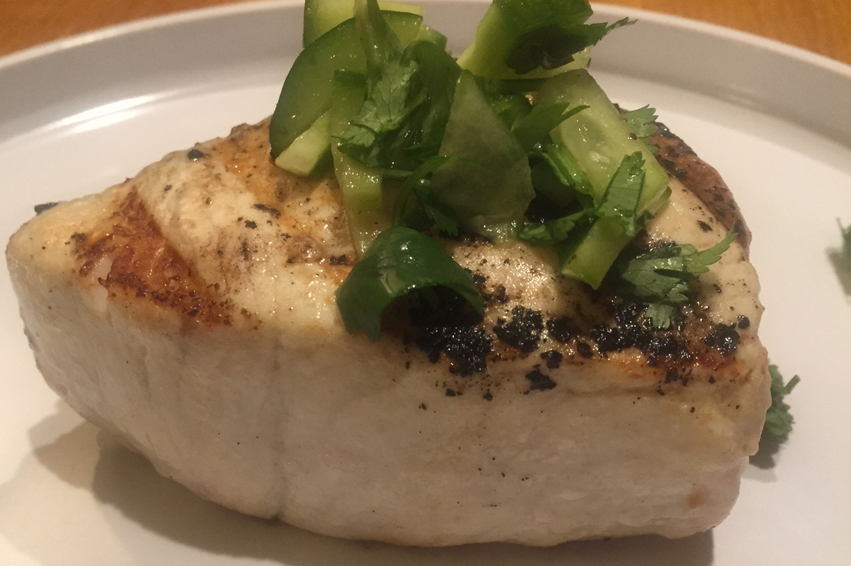 a piece of light fish on a plate with cucumbers on top