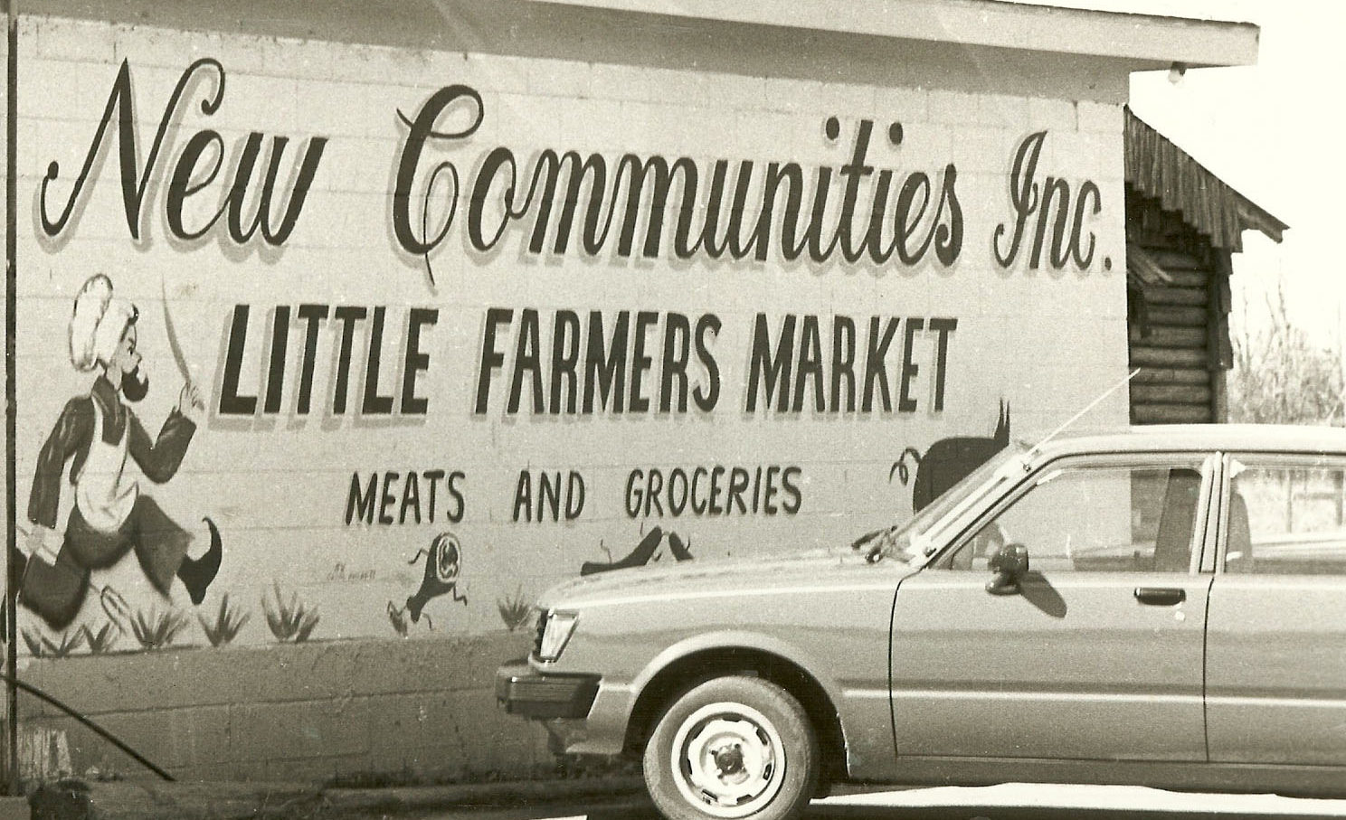 a car parked in front of a wall painted to say "new communities inc. little farmers market"