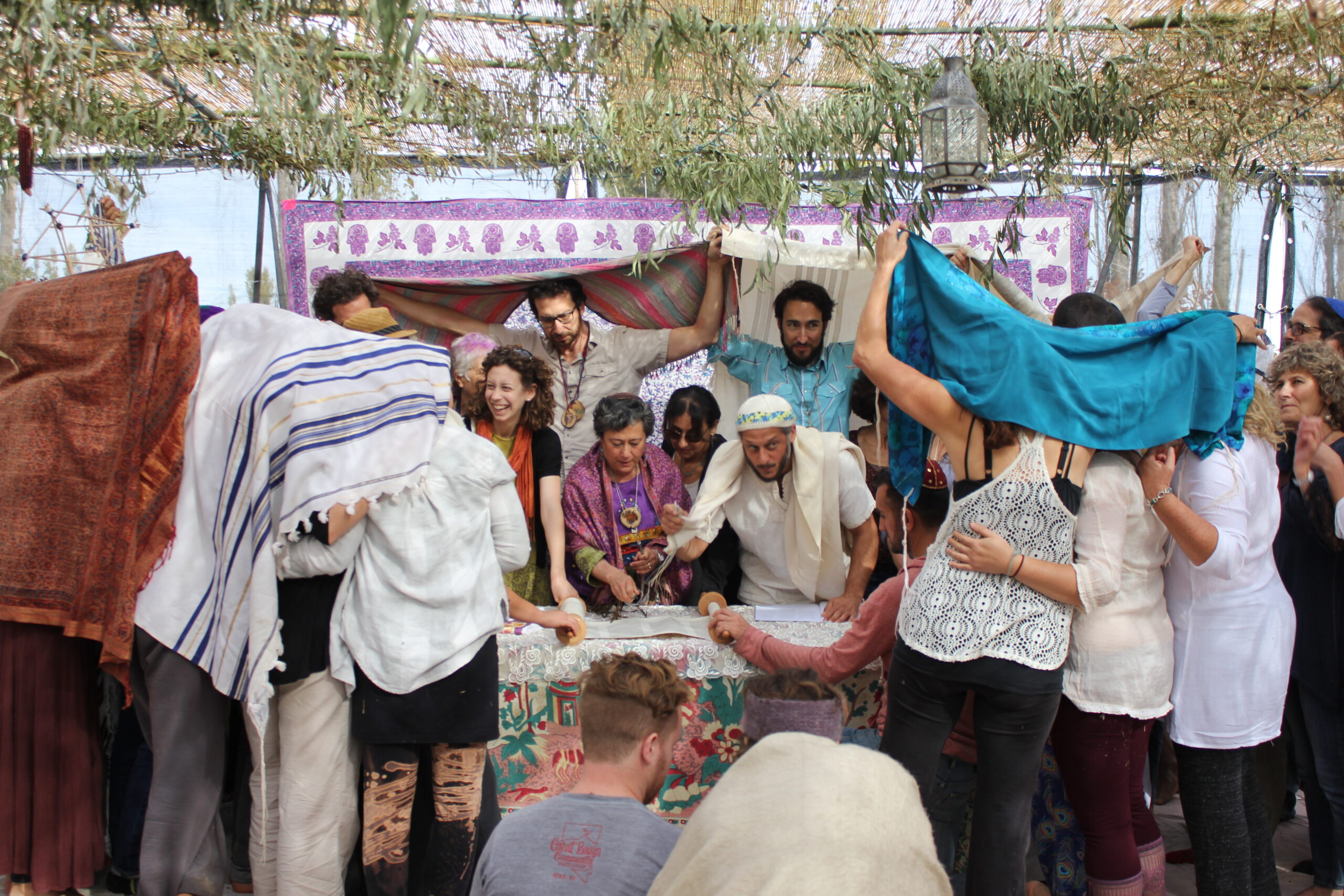 a group of people gather around a torah scroll under a lark sukkah