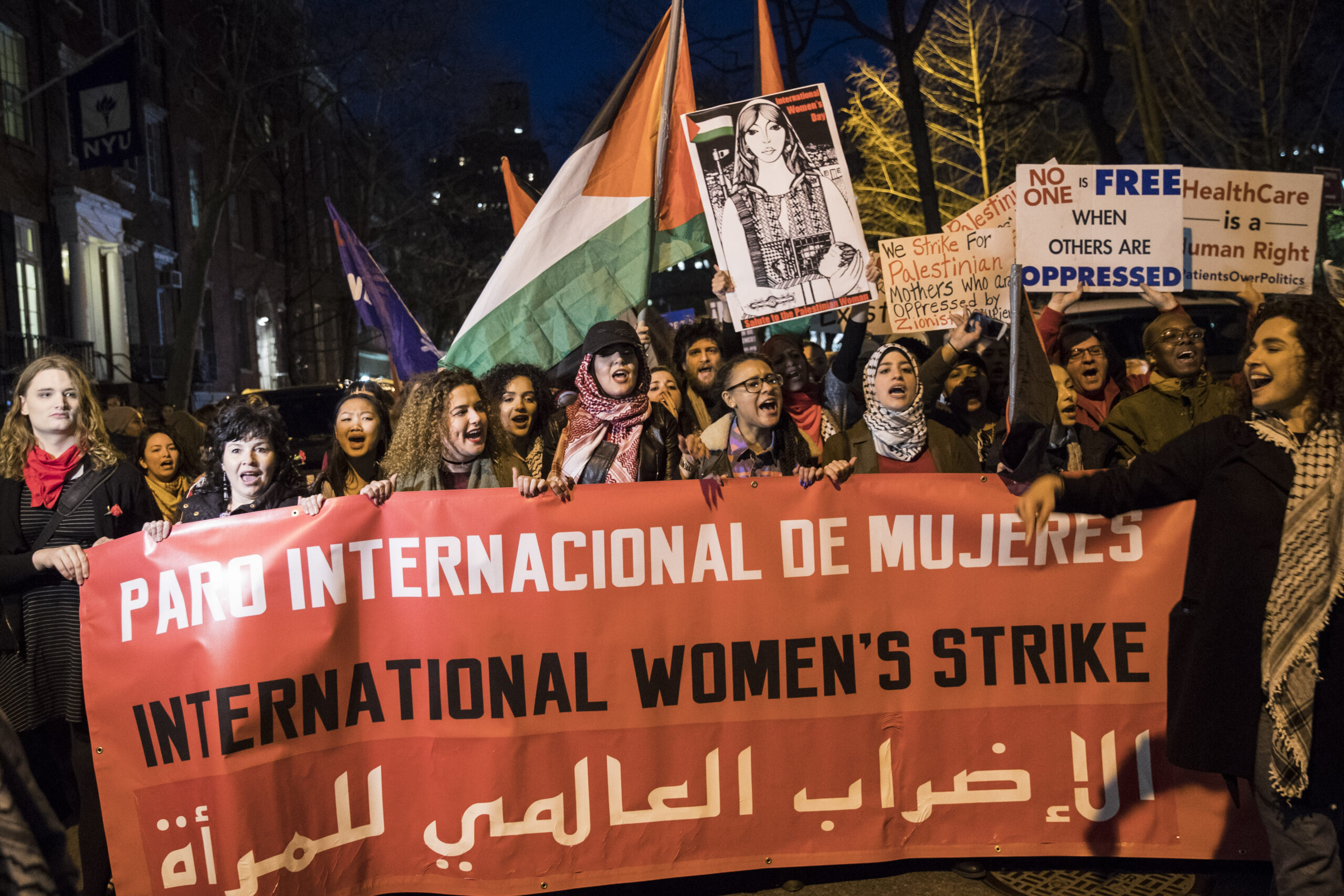 women march with a banner in spanish, english and arabic: "international women's strike"