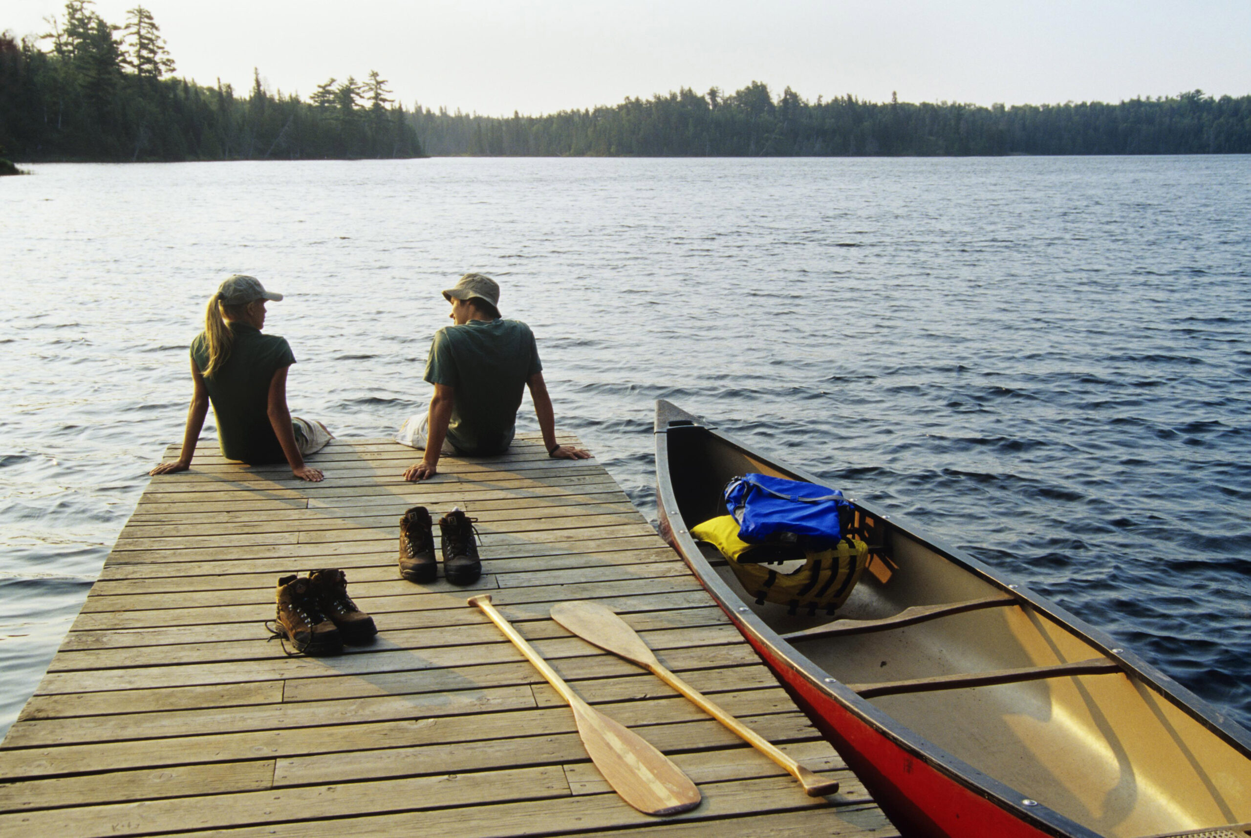 two people sit on the edge of a boat dock