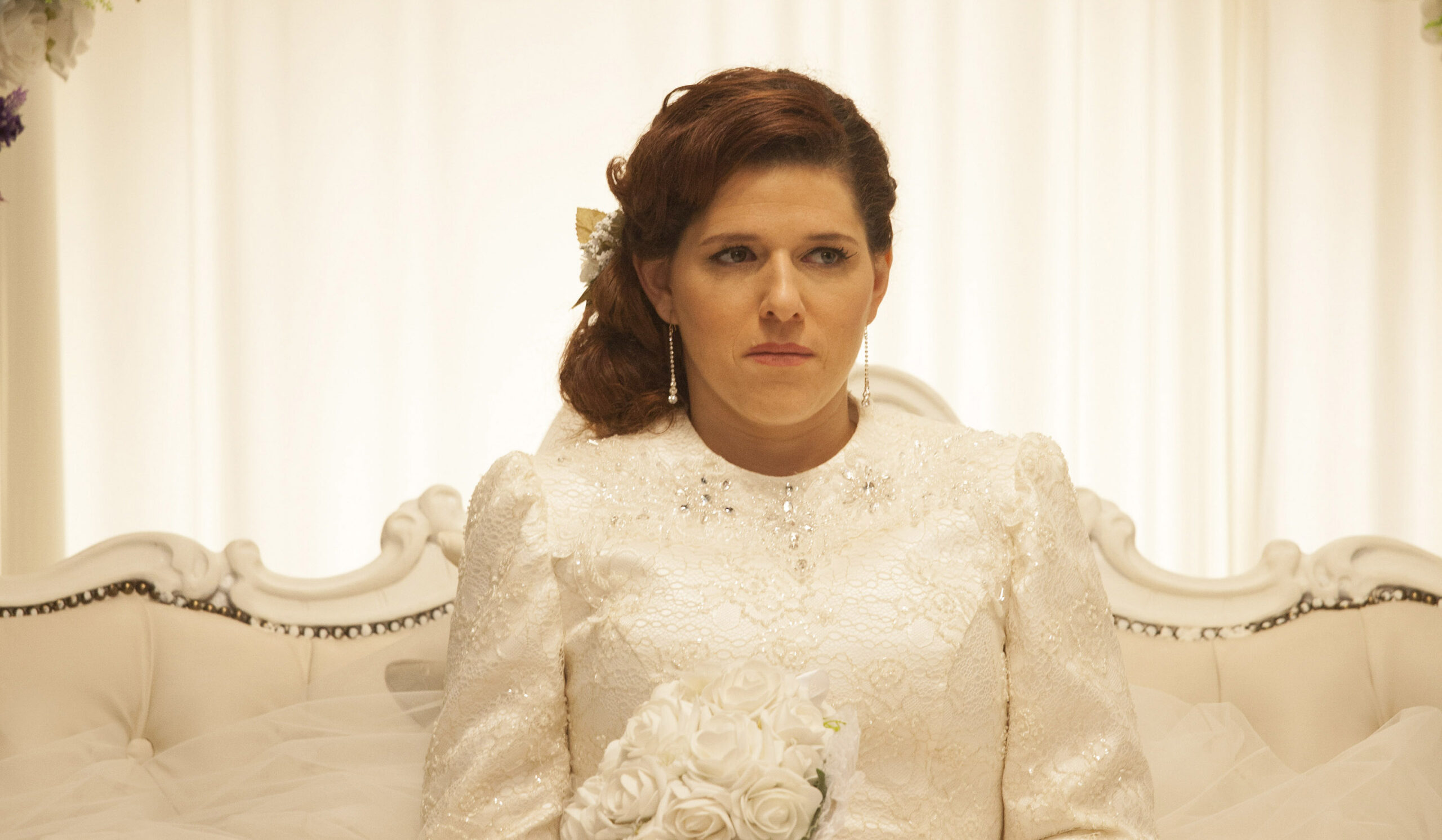 a woman sets in a wedding dress, she looks on the verge of tears