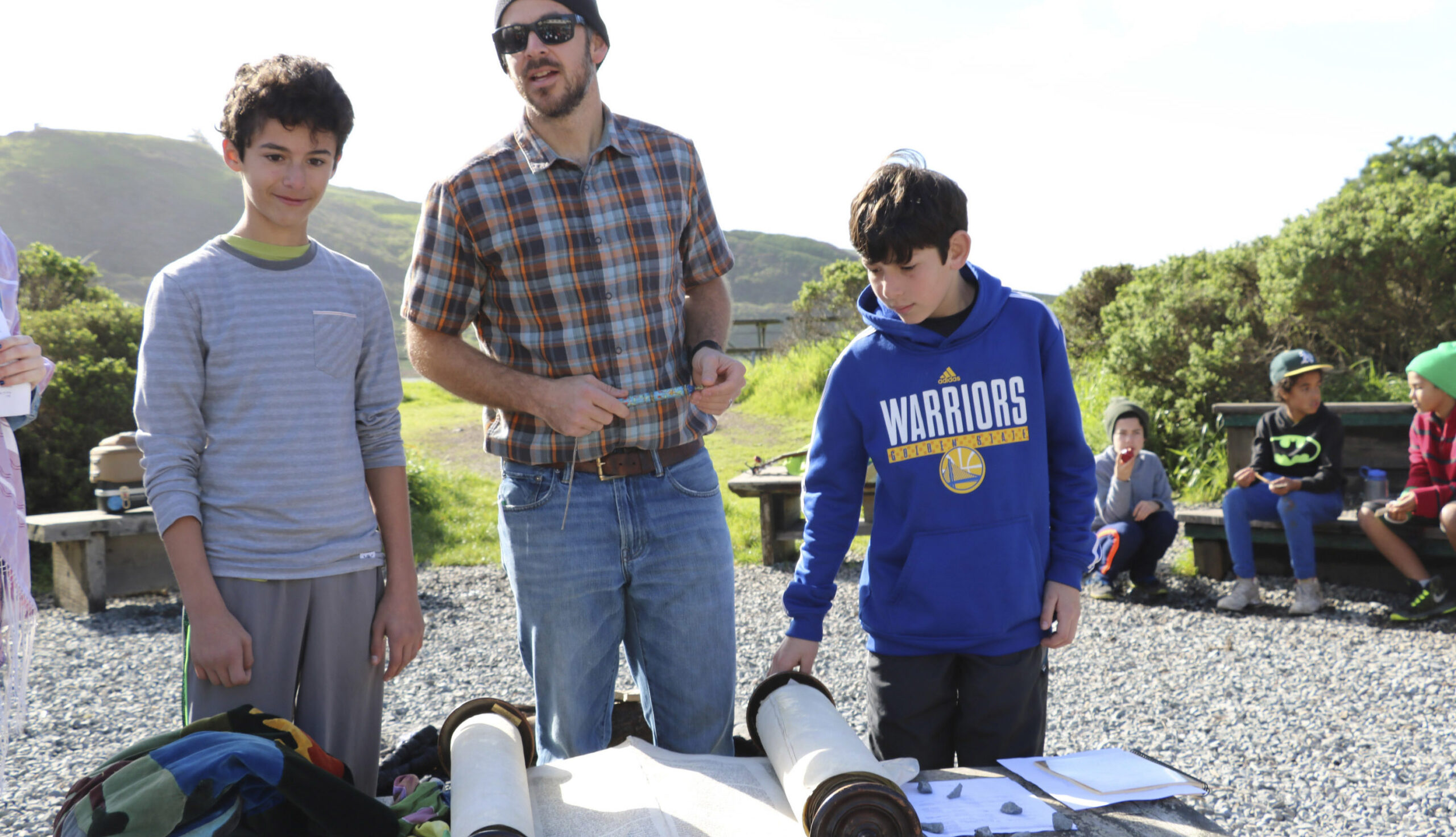 the three of them stand outside in the sun in front of a table with an open torah school on it