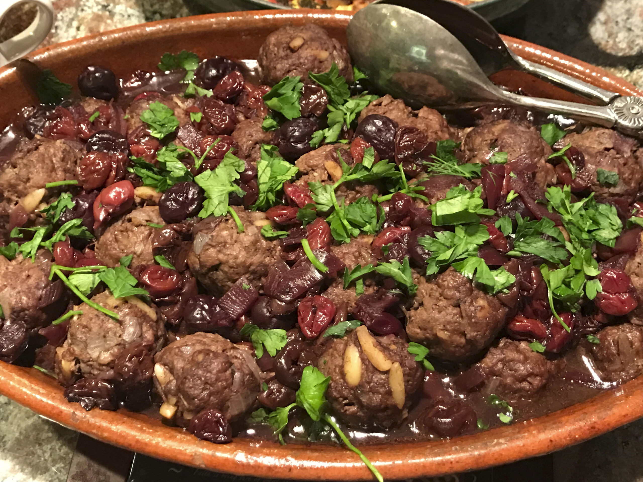 a large pot filled with meatballs and beans, greenery sprinkled on top
