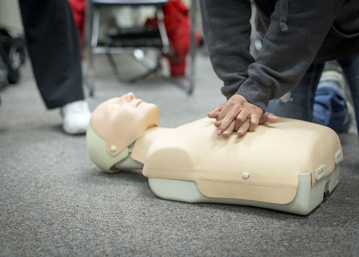 hands with pink nailpolish practice chest compressions on a CPR dummy on the floor