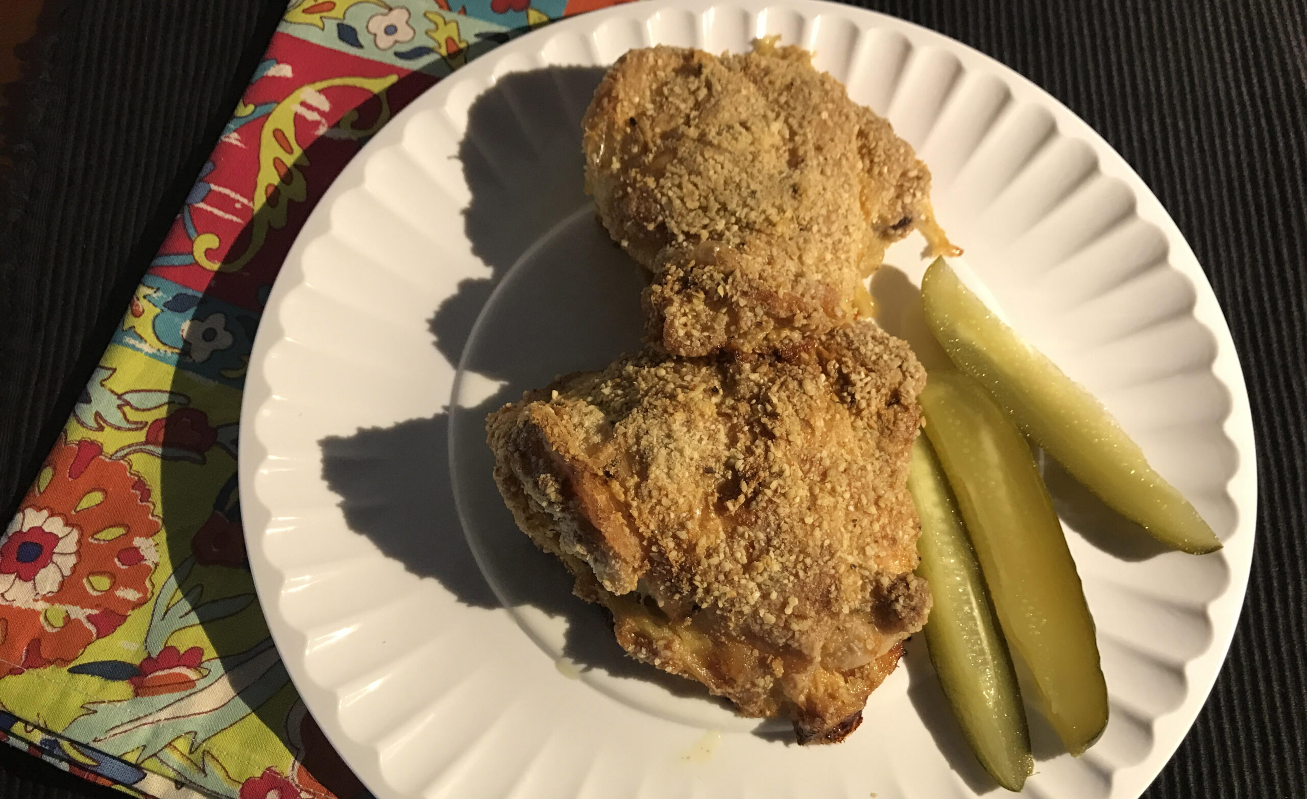 paper plate in the sun with fried chicken and pickles on it