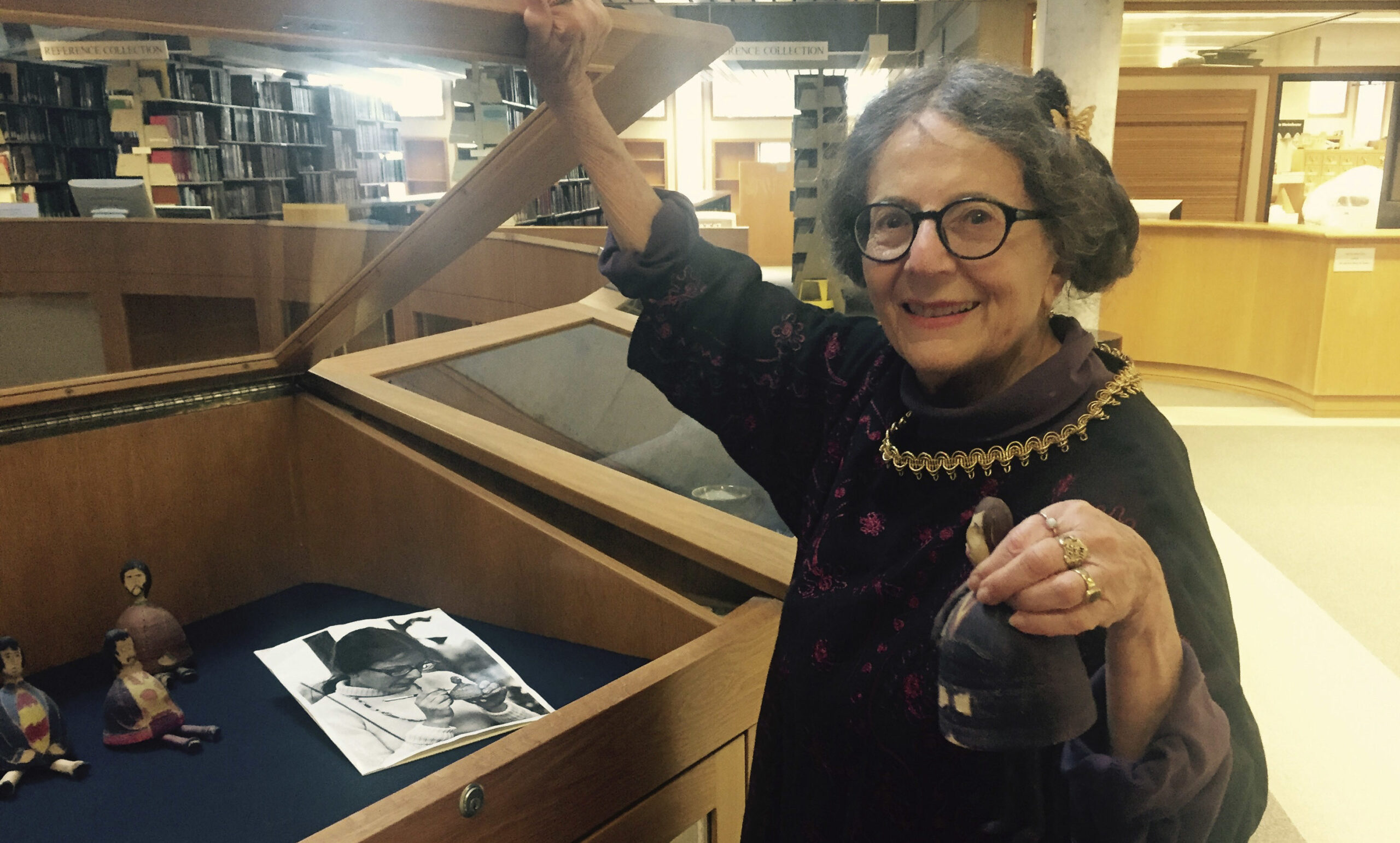 she holds open a display case and holds up one of the beatle bells for the camera to see