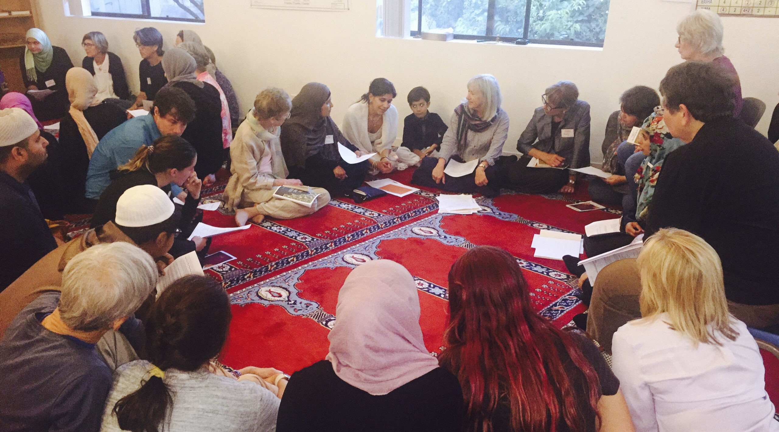 people sit in a circle on red rugs on the floor