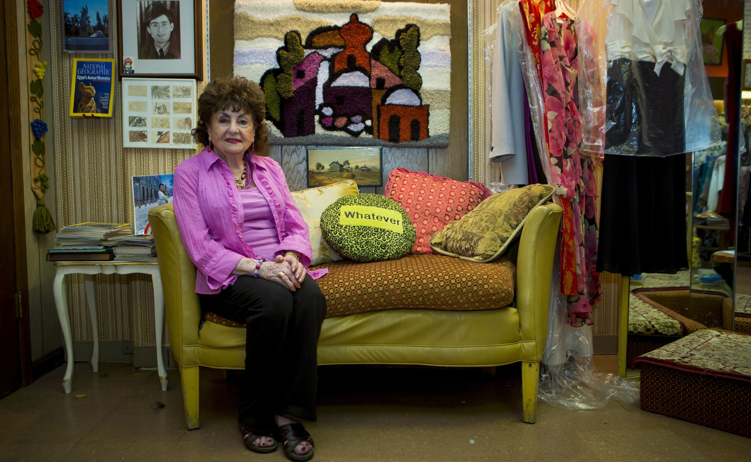 Sonia is an older woman, seated in a bright pink top on the sofa, next to her is a bright green pillow that says "whatever"