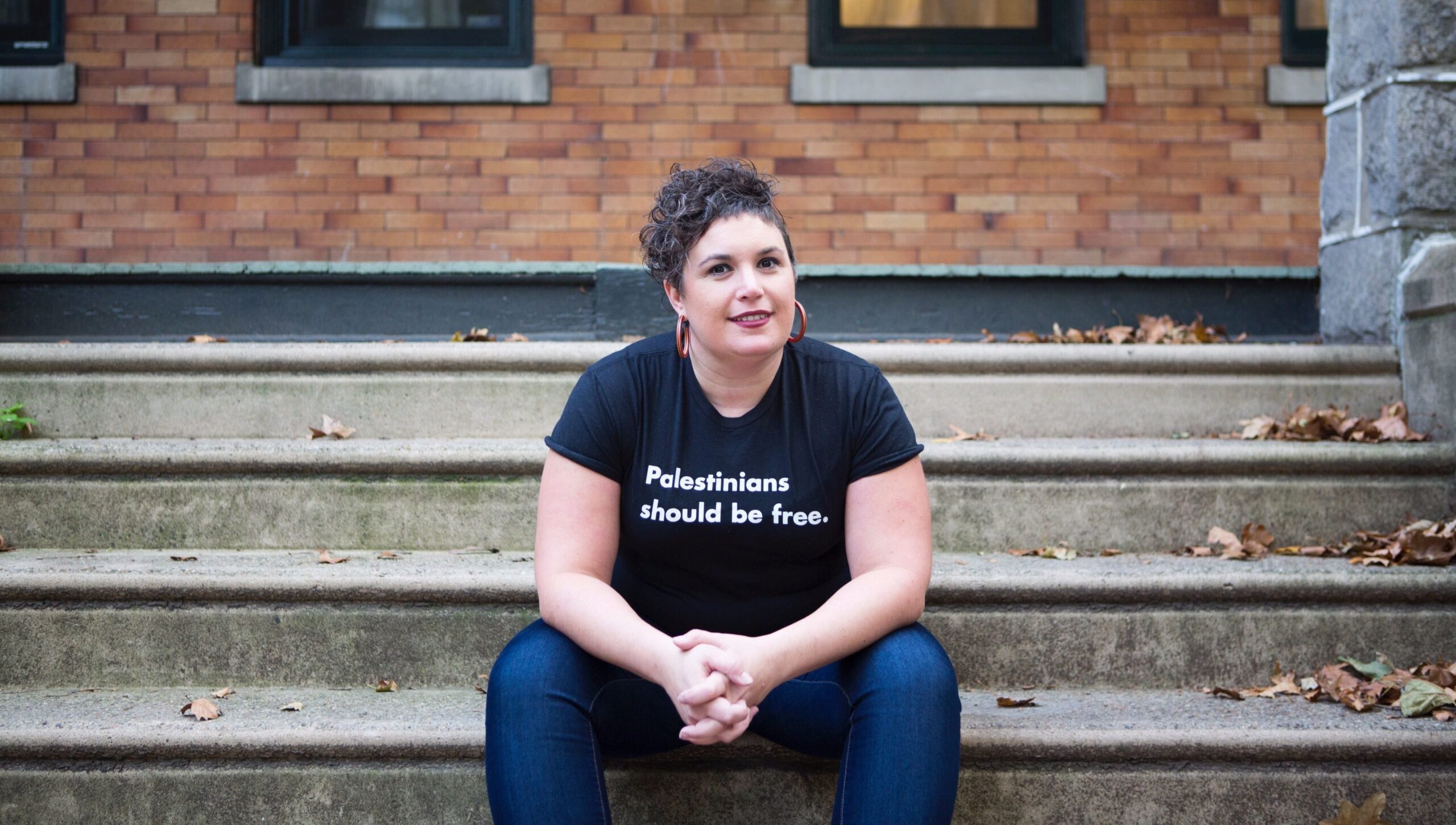 Rabbi Alissa Wise sits on steps with a shirt that says "Palestinians should be free"