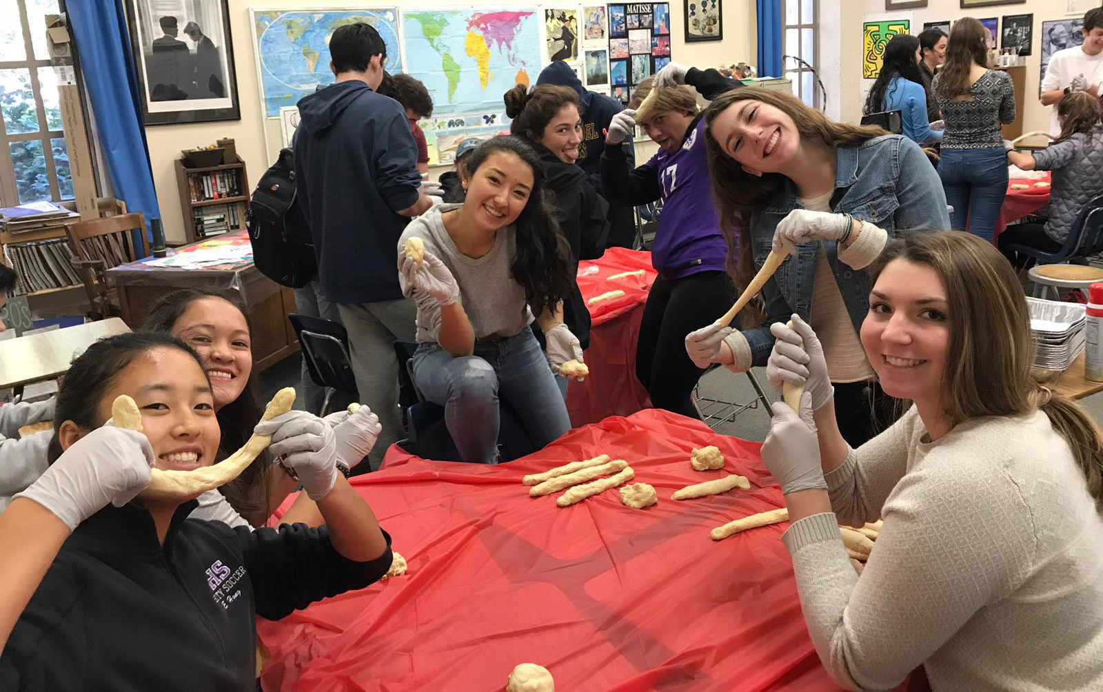 a group of teen girls smile and hold up challah braids in progress