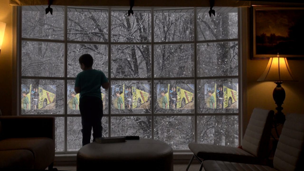 the silhouette of a person looking out a window. there is snow falling outside.