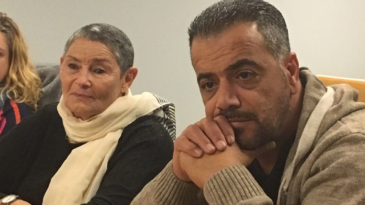 A man and a woman sit next to each other, looking solemn