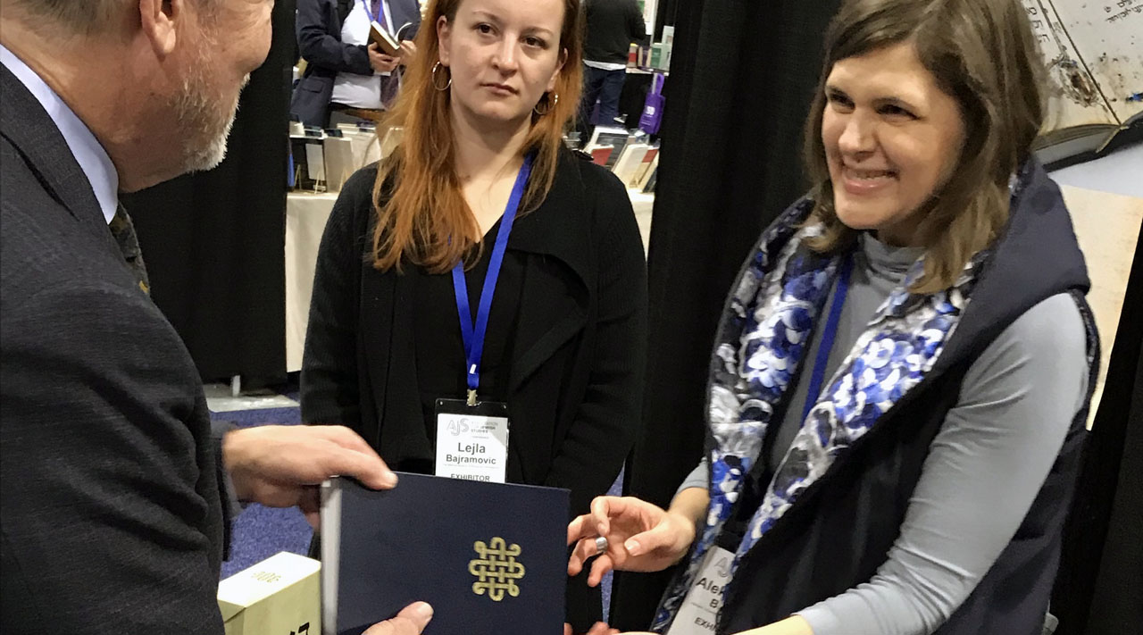 a smiling woman hands a man a book