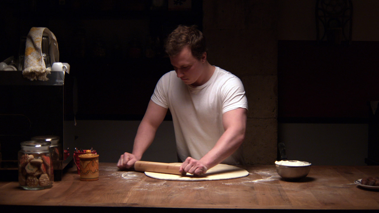 a young blond man rolls out dough with a rolling pin