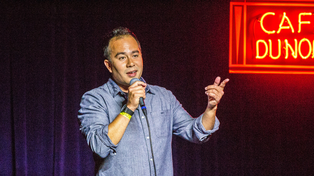 an Asian man stands on a stage holding a mic