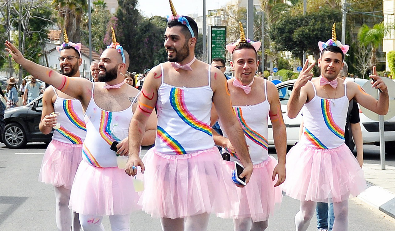 five men walk down the street in pink tutus, rainbow t-shirts, and unicorn horns