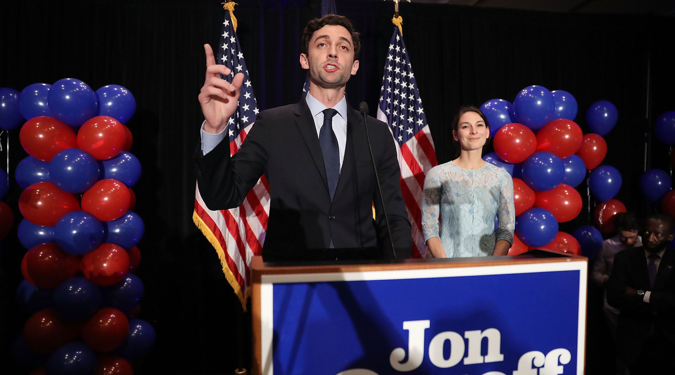 a white man in a suit speaks at a prodium