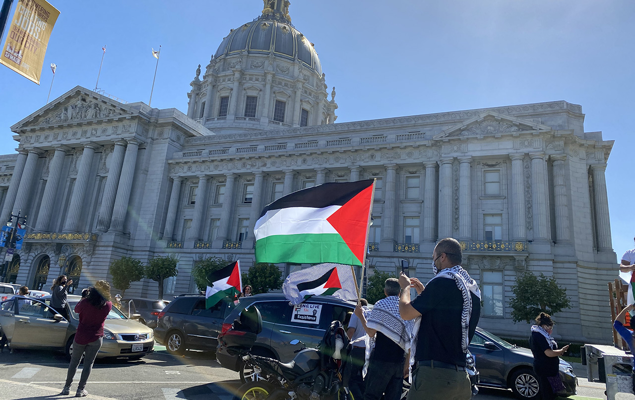 cars and people with Palestinians flags in front of city hall