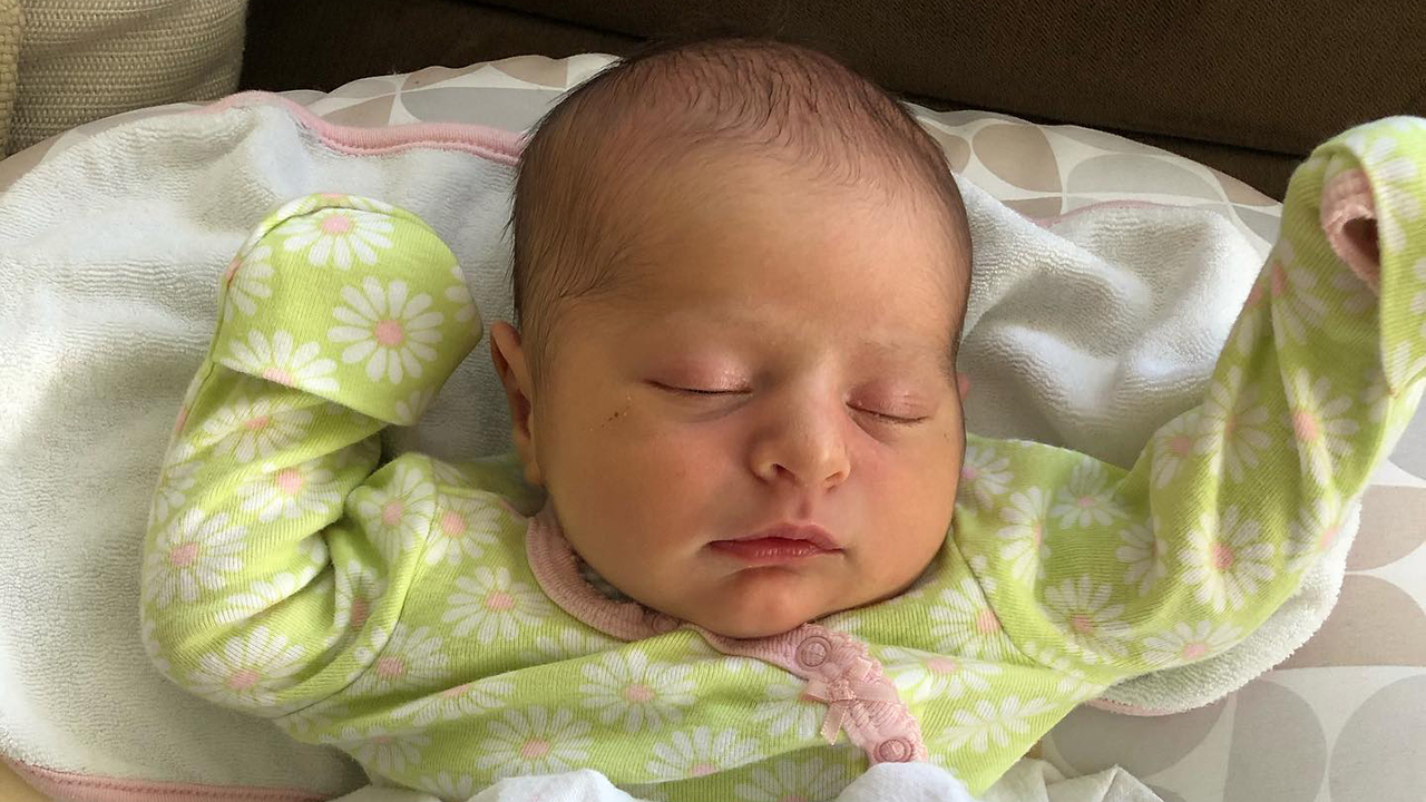 a newborn baby sleeping in a green floral onesie