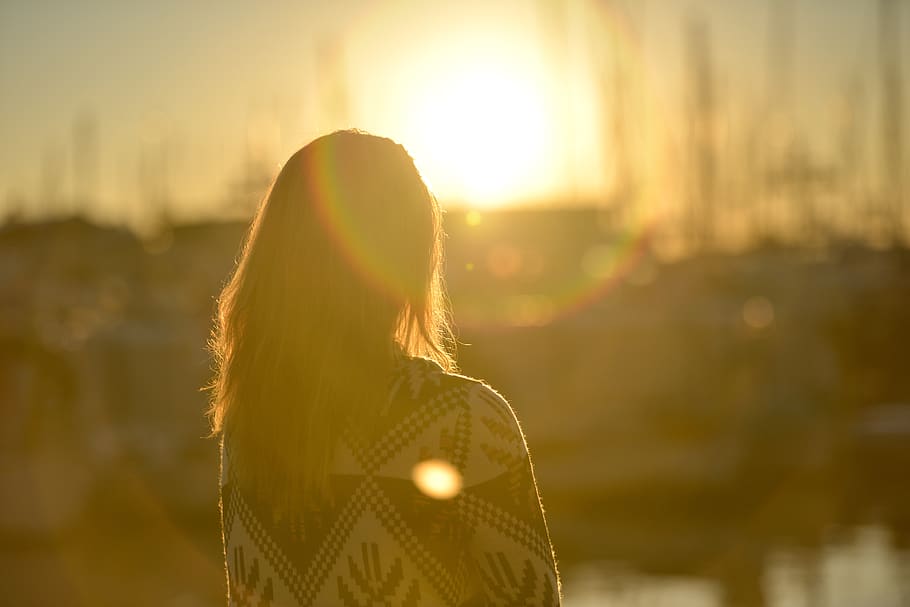 a woman in silhouette looks toward a sunset
