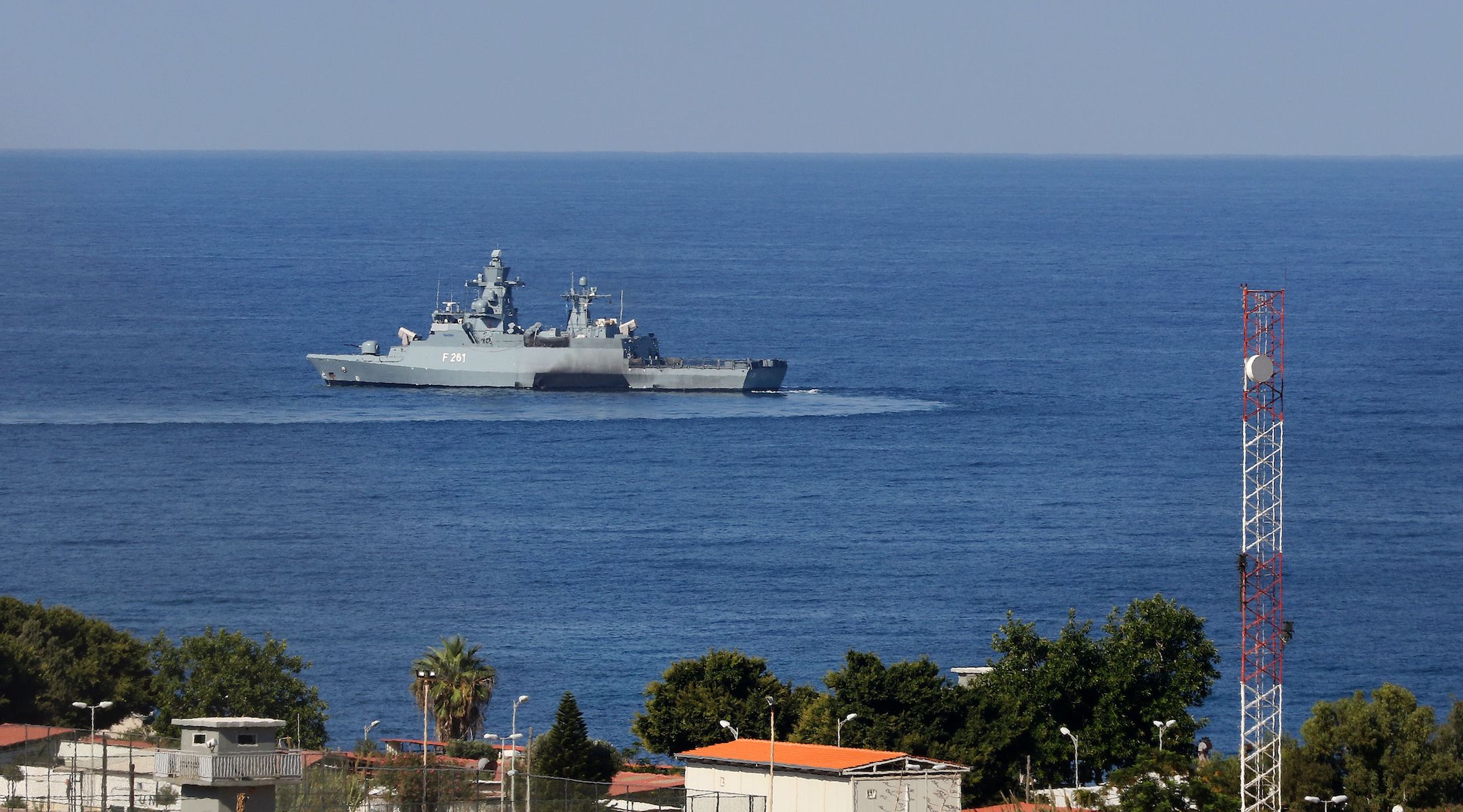 A view over some rooftops to the open sea and a grey military-looking vessel
