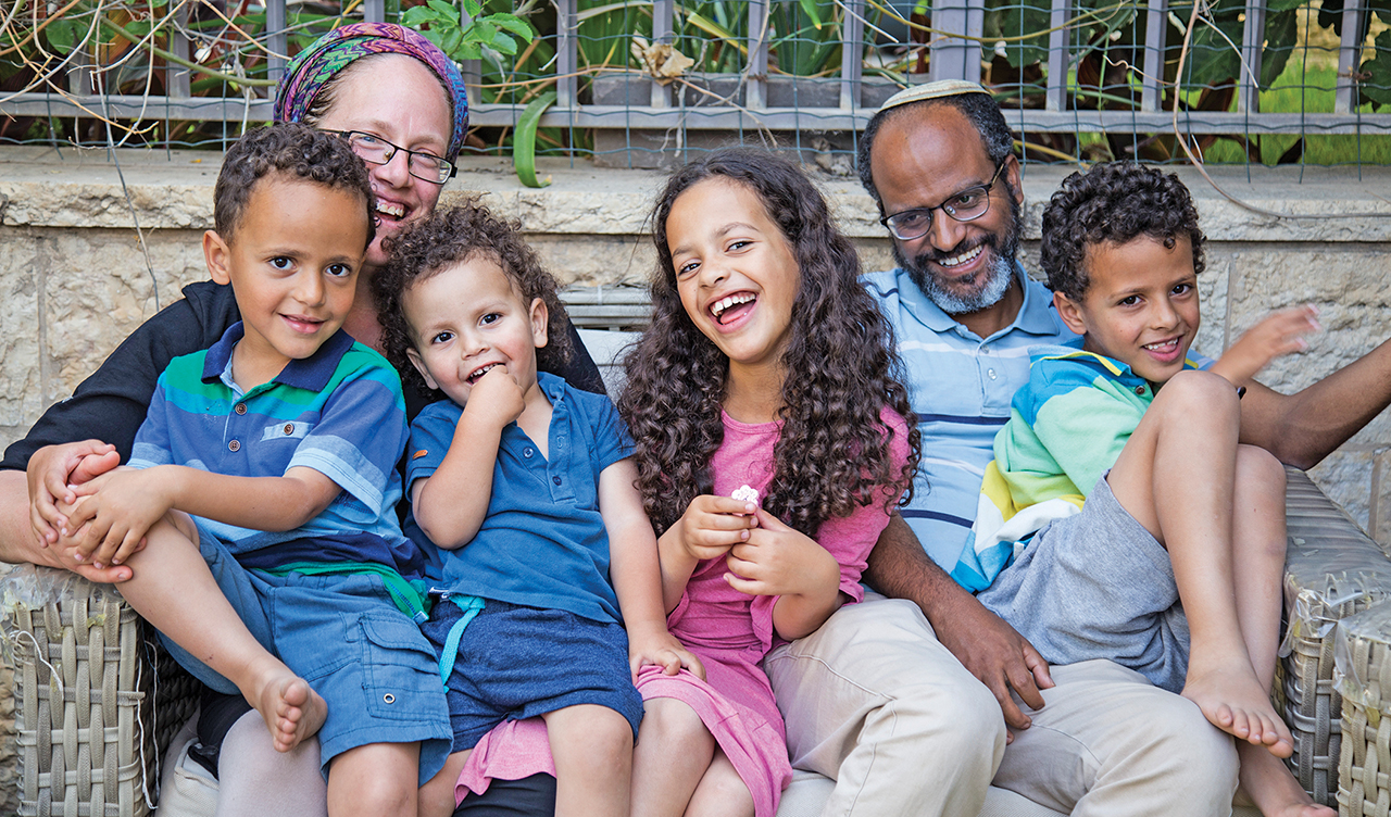 A family of six — a white woman, a Black man, and a gaggle of kids — pose for a portrait