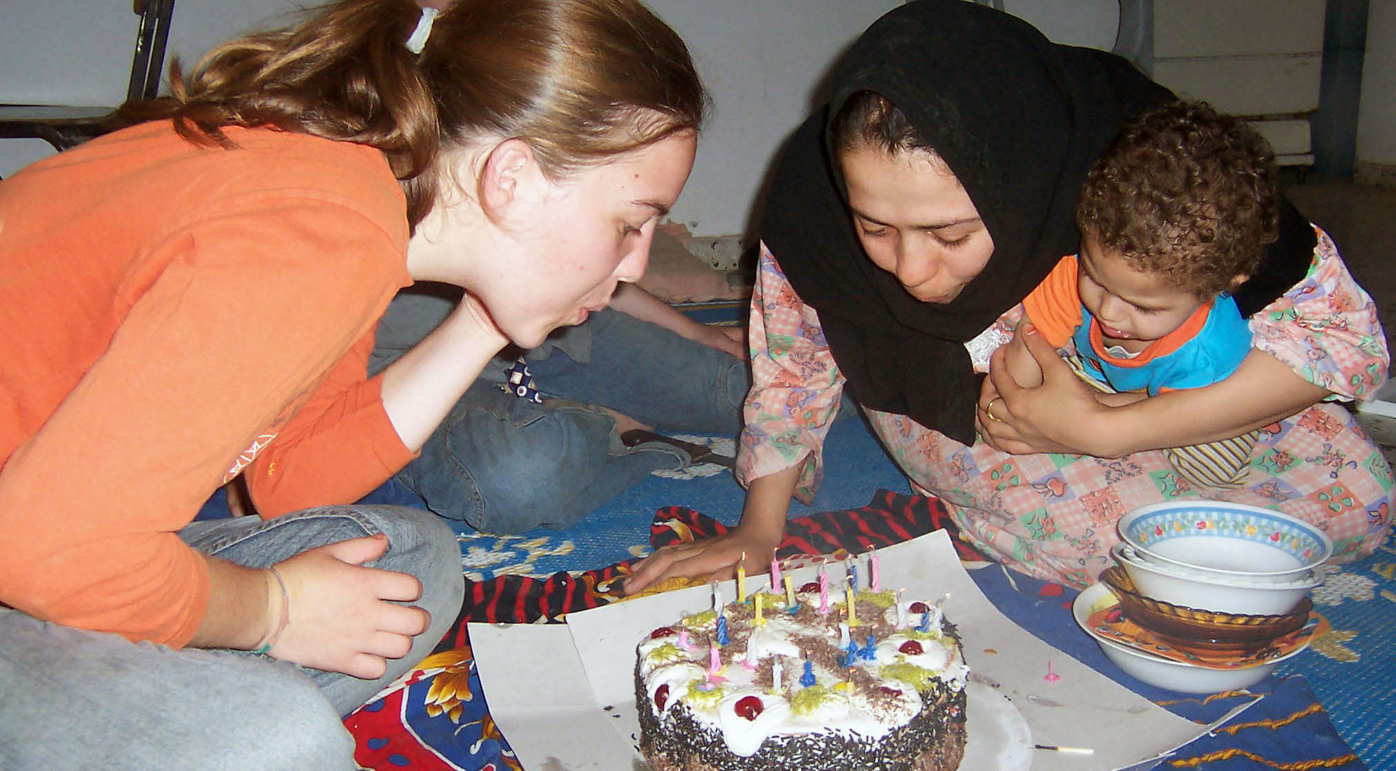 Two women blow out birthday candles, as one woman holds an infant