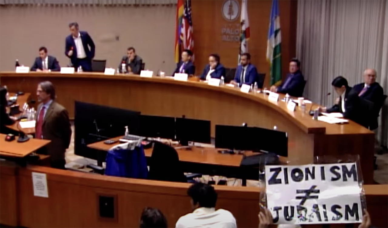 A protester holds up a sign that says "Zionism does not equal Judaism" during a Jan. 31 forum for congressional candidates in Palo Alto. (Screenshot)