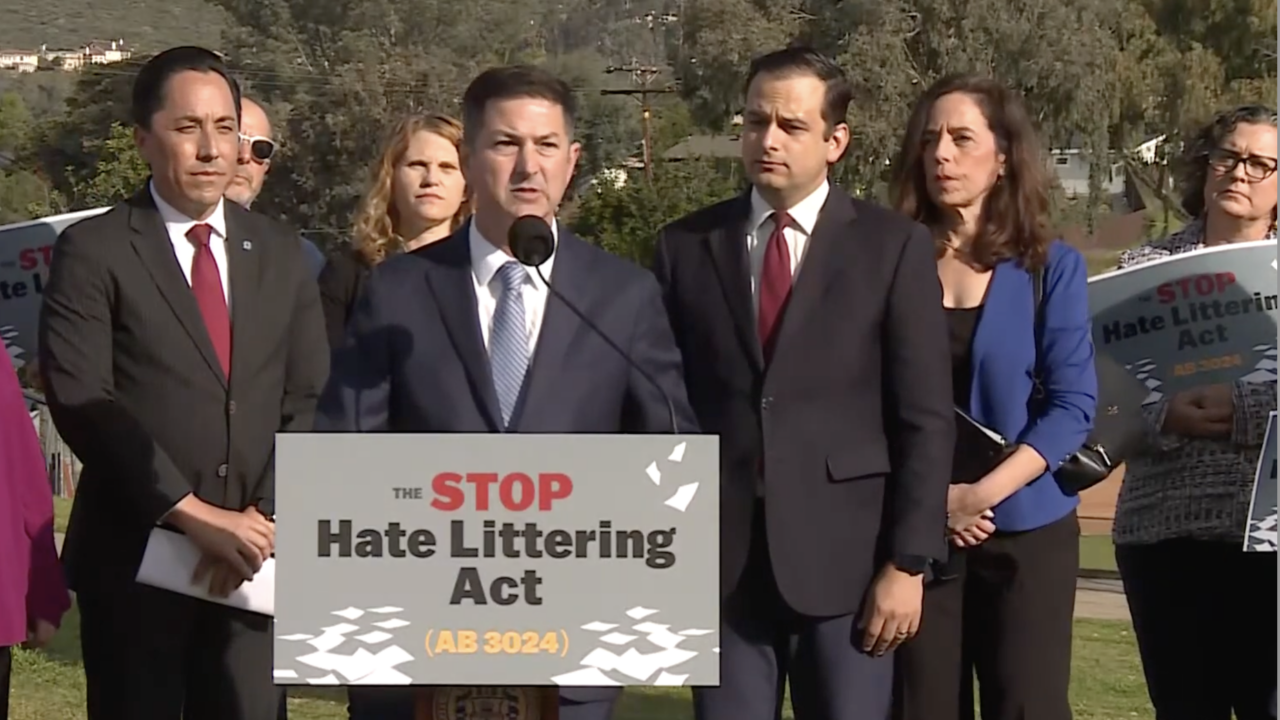 Man speaks at podium surrounded by others