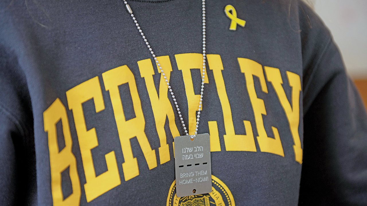 close up of a Berkeley sweatshirt with a yellow ribbon pin and a "Bring Them Home" dog tag worn over it