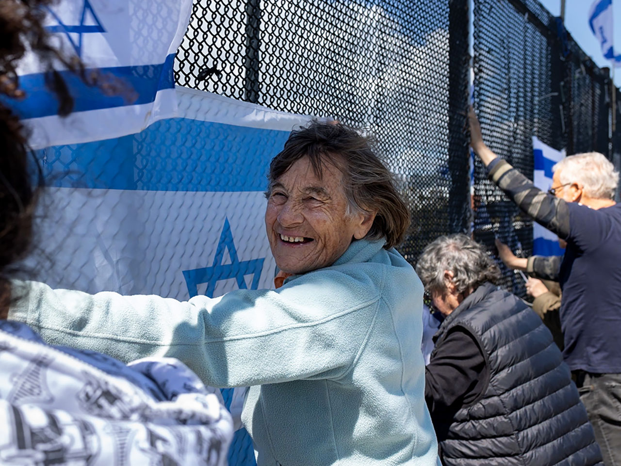 Bella Barany, 87, a Berkeley resident who told J. she is making aliyah soon to join her daughter in Israel, flashes a smile as she holds an Israeli flag on a pedestrian overpass in Berkeley in support of the hostages in Gaza, May 5, 2024. (Photo/Ido Bartana)