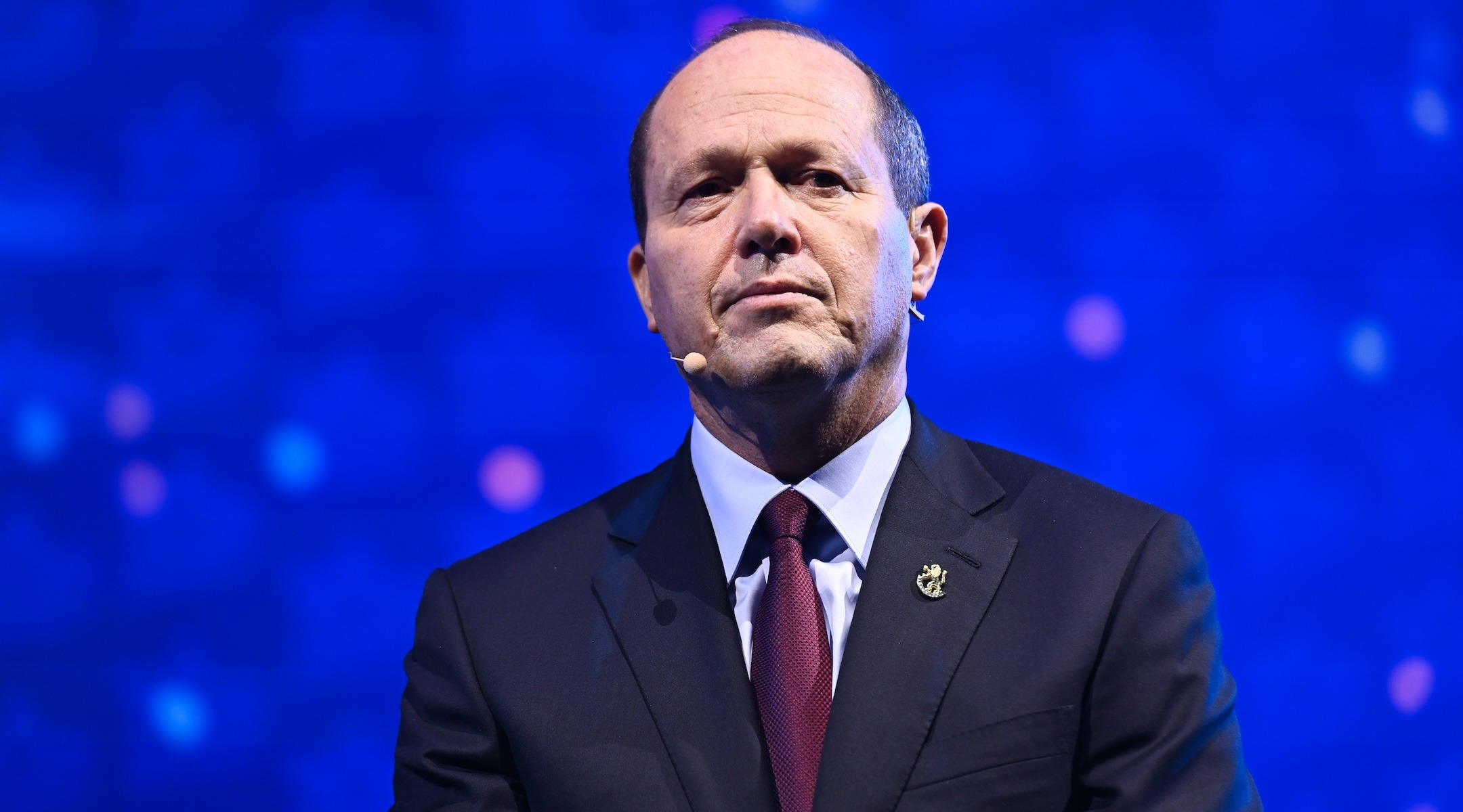 a balding man in a suit stands stoically