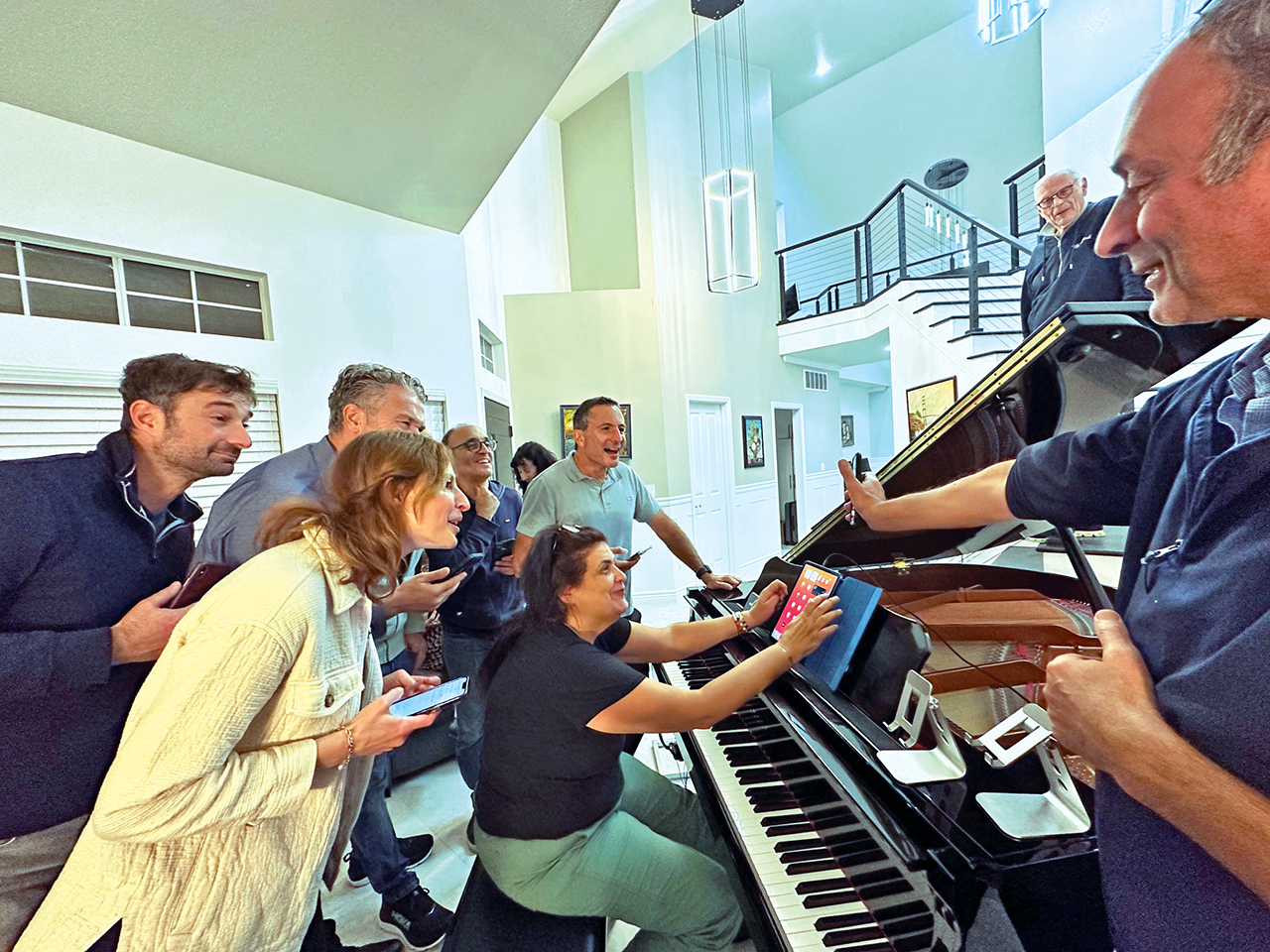 Several men and women crowd around a piano while a man plays