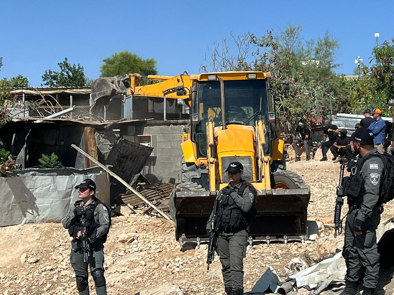Israel Defense Forces personnel stand guard as a bulldozer demolishes a building in the Palestinian village of Umm al-Khair in the West Bank on June 26, 2024. (Eid Suleiman)