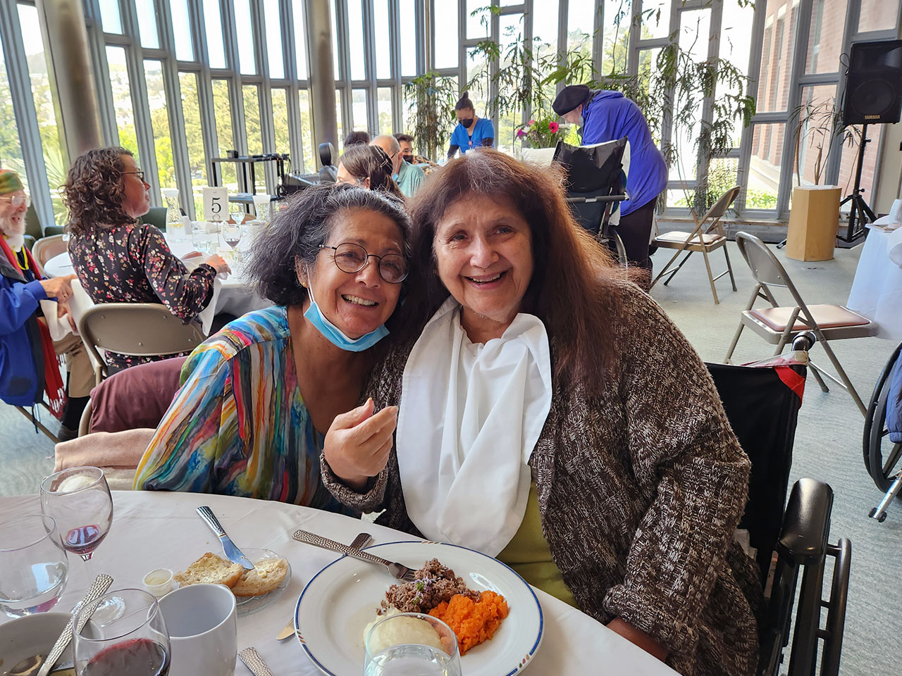 Two women sit together in a sunny dining hall