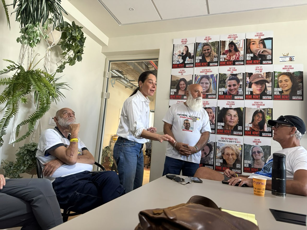 a woman stands in a small conference room speaking to a handful of seated men