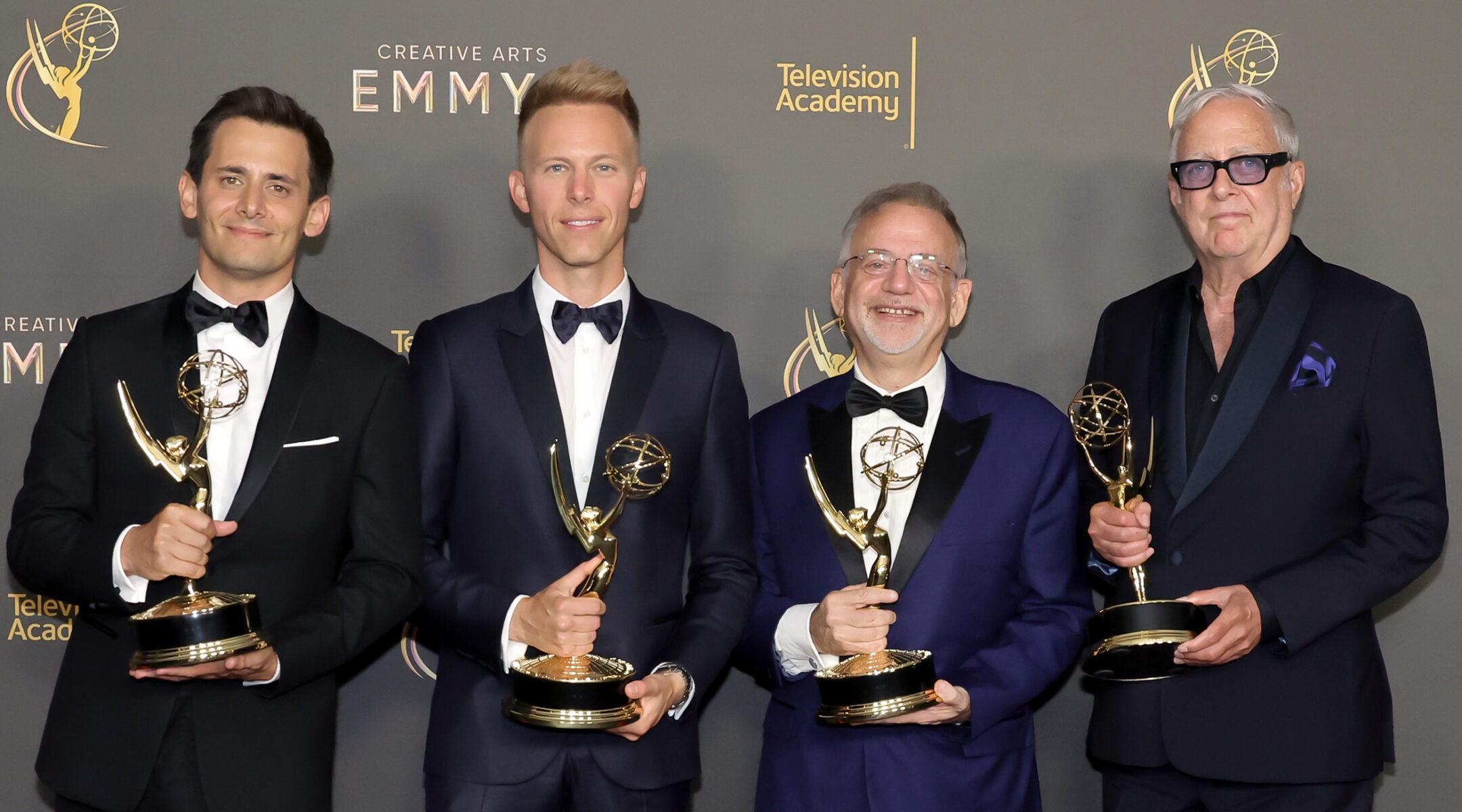 four men in tuxes stand holding their golden Emmy statues