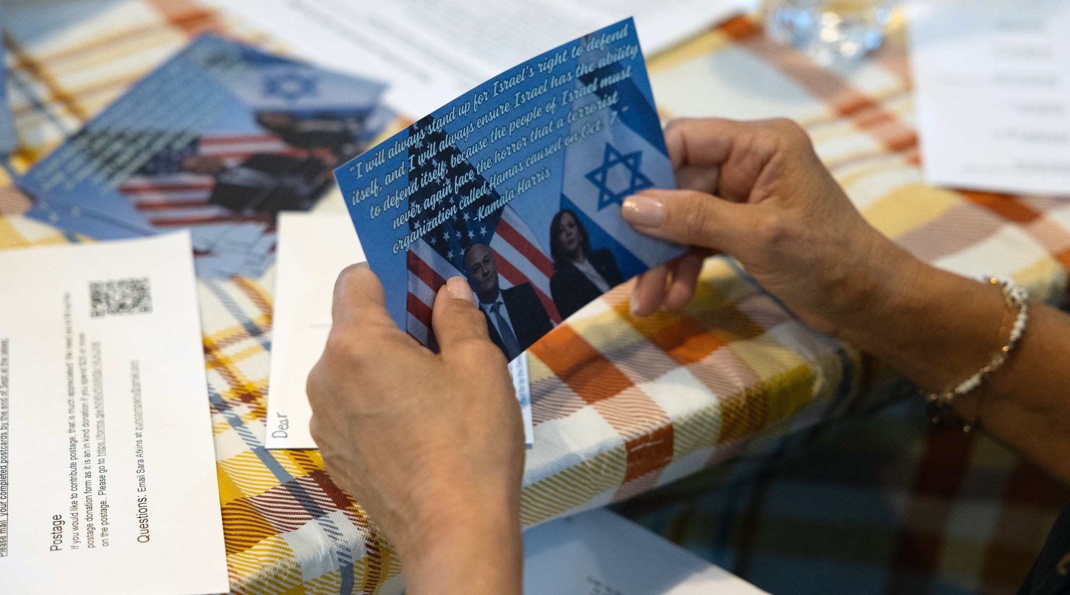 a woman's hands hold a postcard with a picture of Harris and Emhoff on it