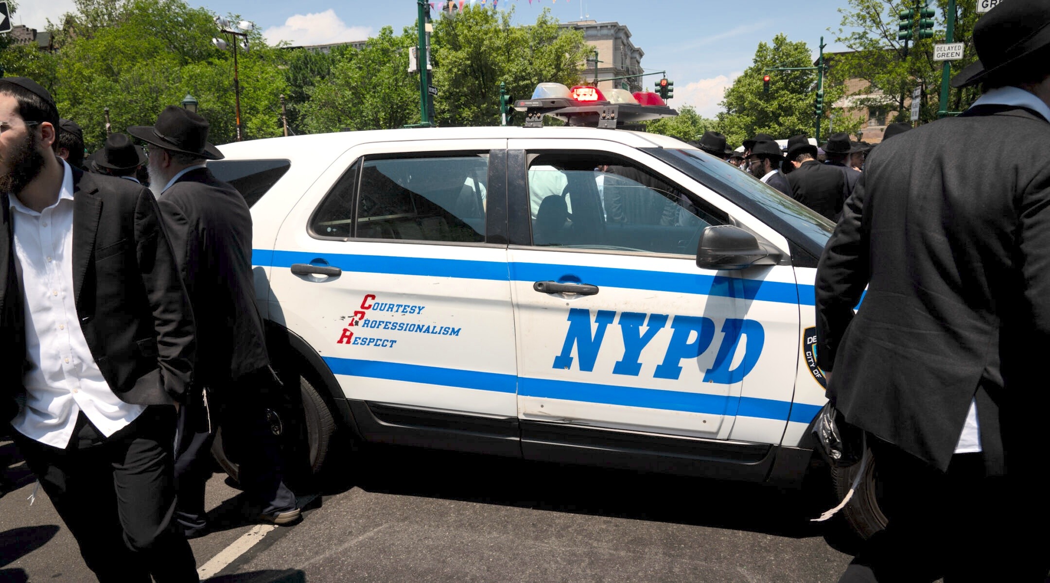 Men Hasidic dress stand near an NYPD car