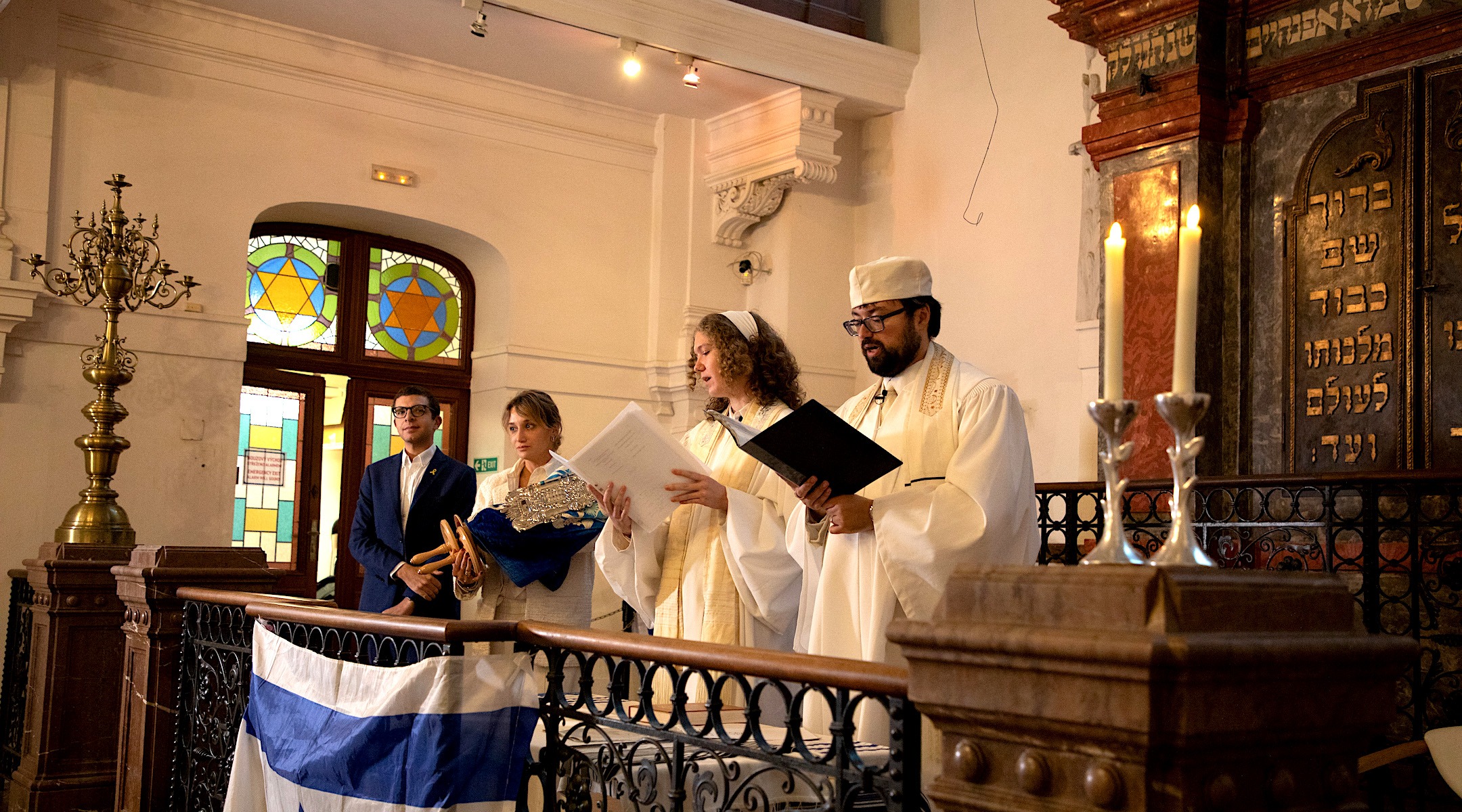 A man and woman in white cantorial robes stand on the bimah, with two others holding a Torah off to the side