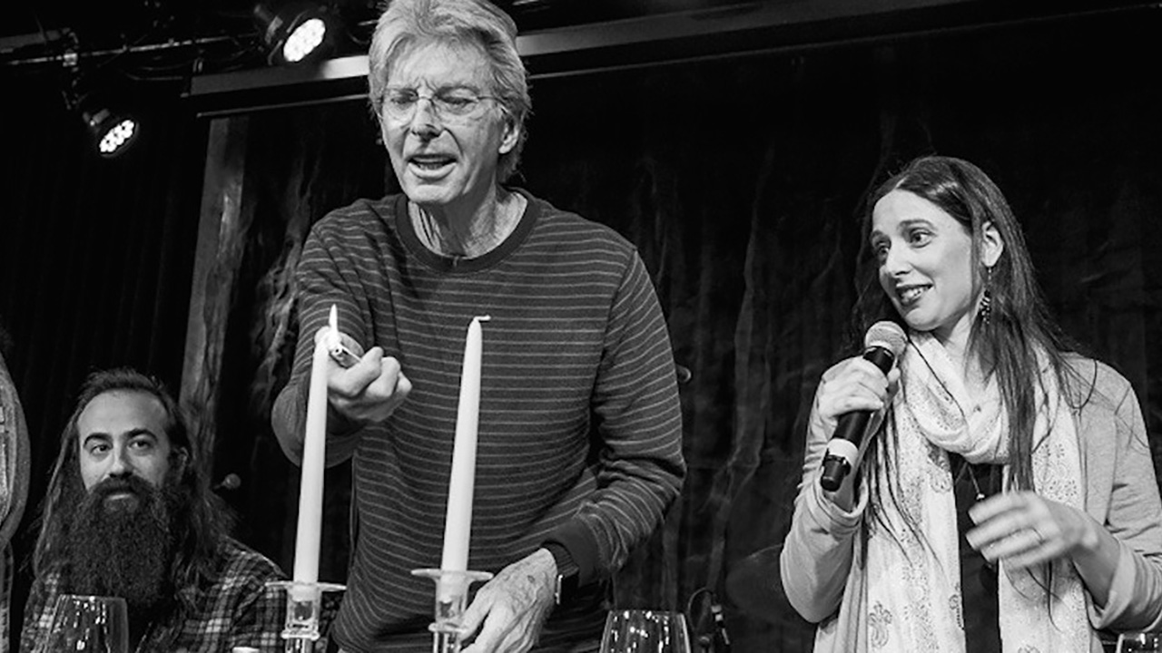 black and white photo of a man lighting two tall candles. a woman stands next to him holding a microphone.