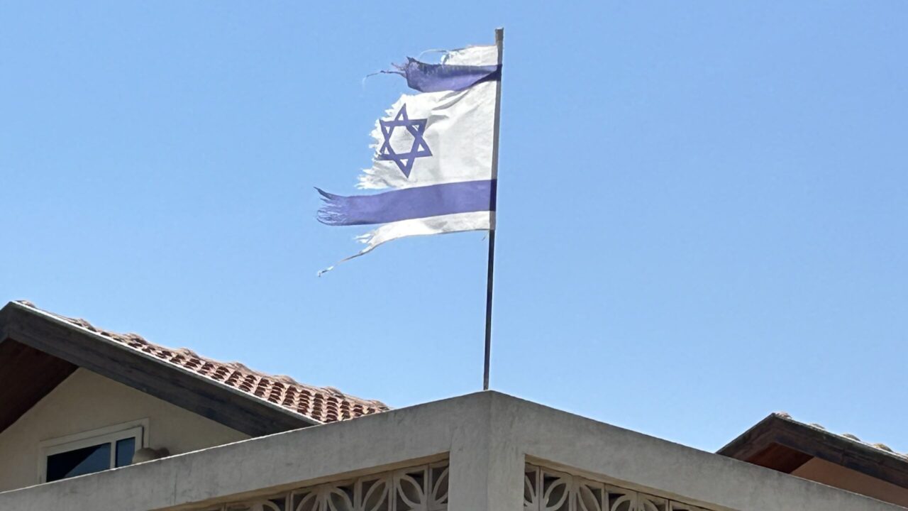 a tattered Israeli flag waves from the top of a residential building