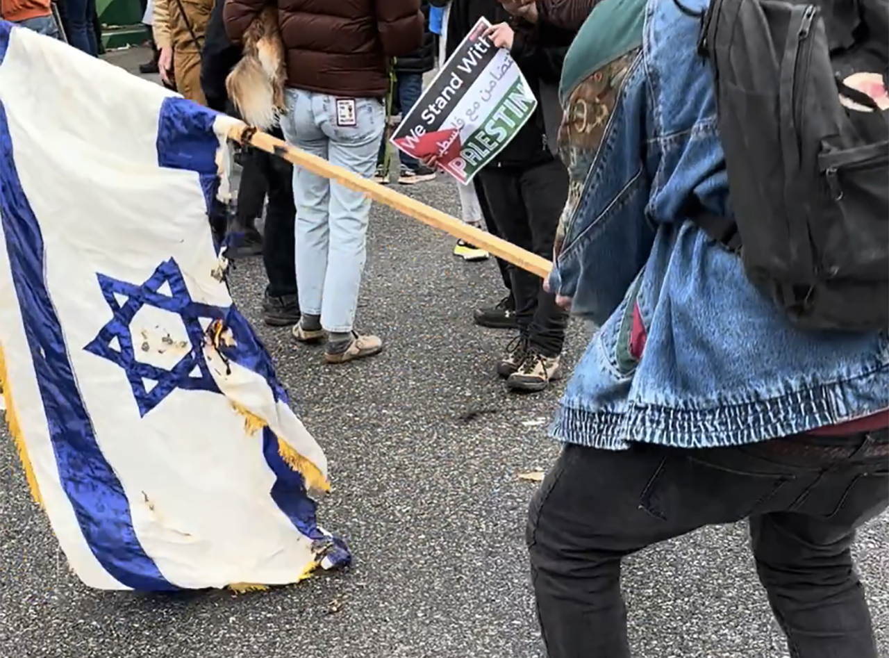 A screenshot from video captured at the scene shows a masked man holding the flag as it smolders.