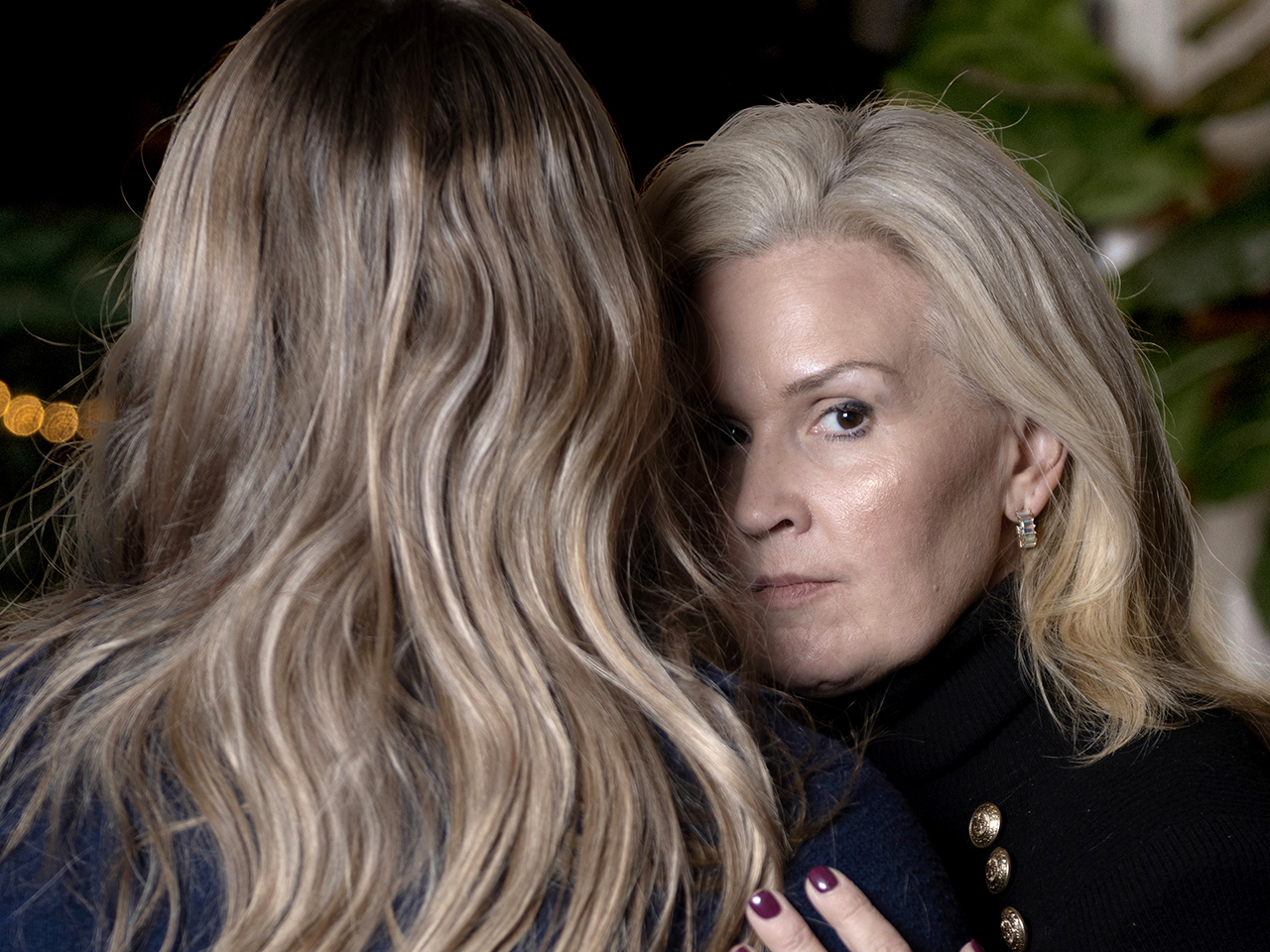 a blond woman hugs her daughter, who is seen only from behind