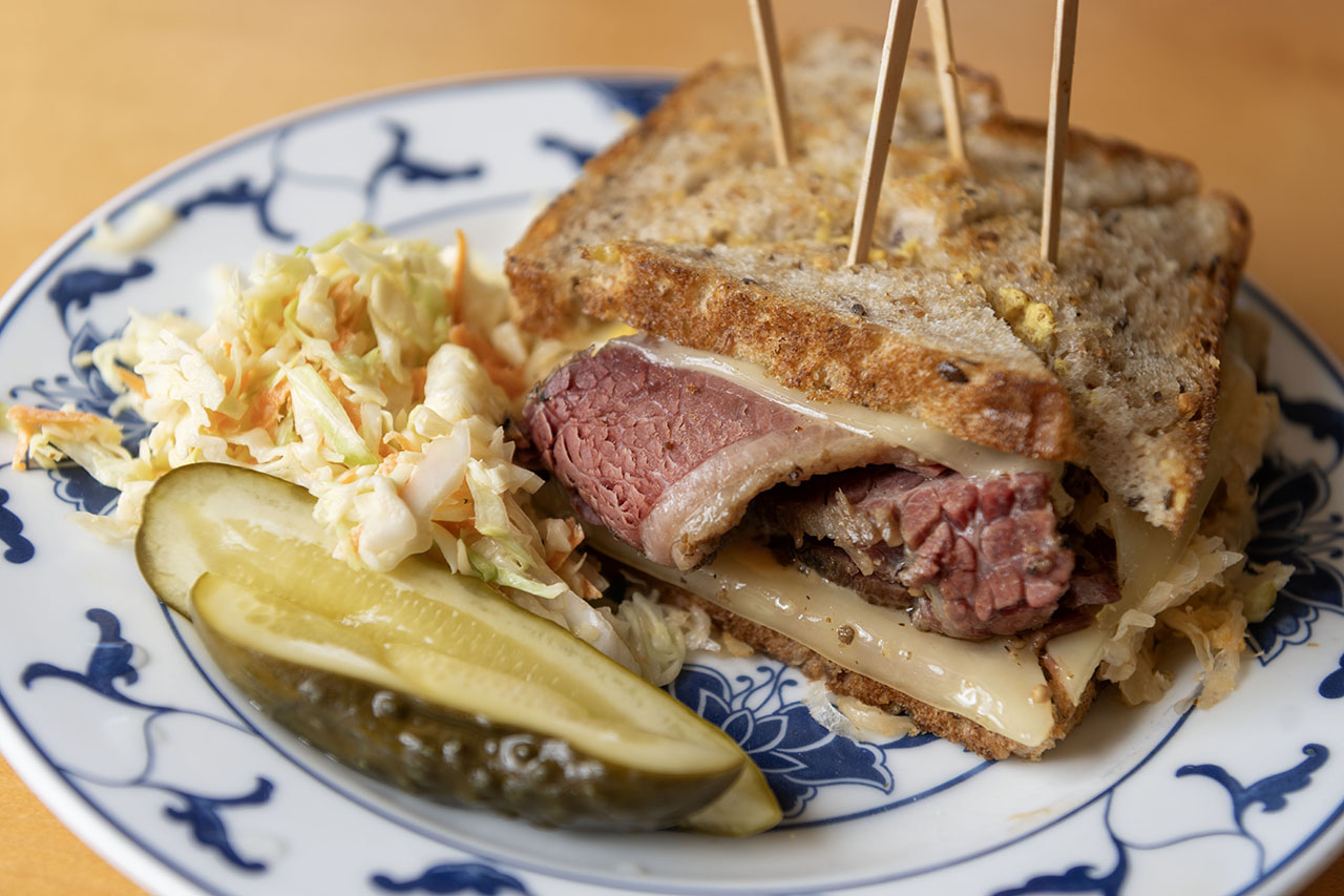 a pastrami sandwich on a plate with a pickle and coleslaw