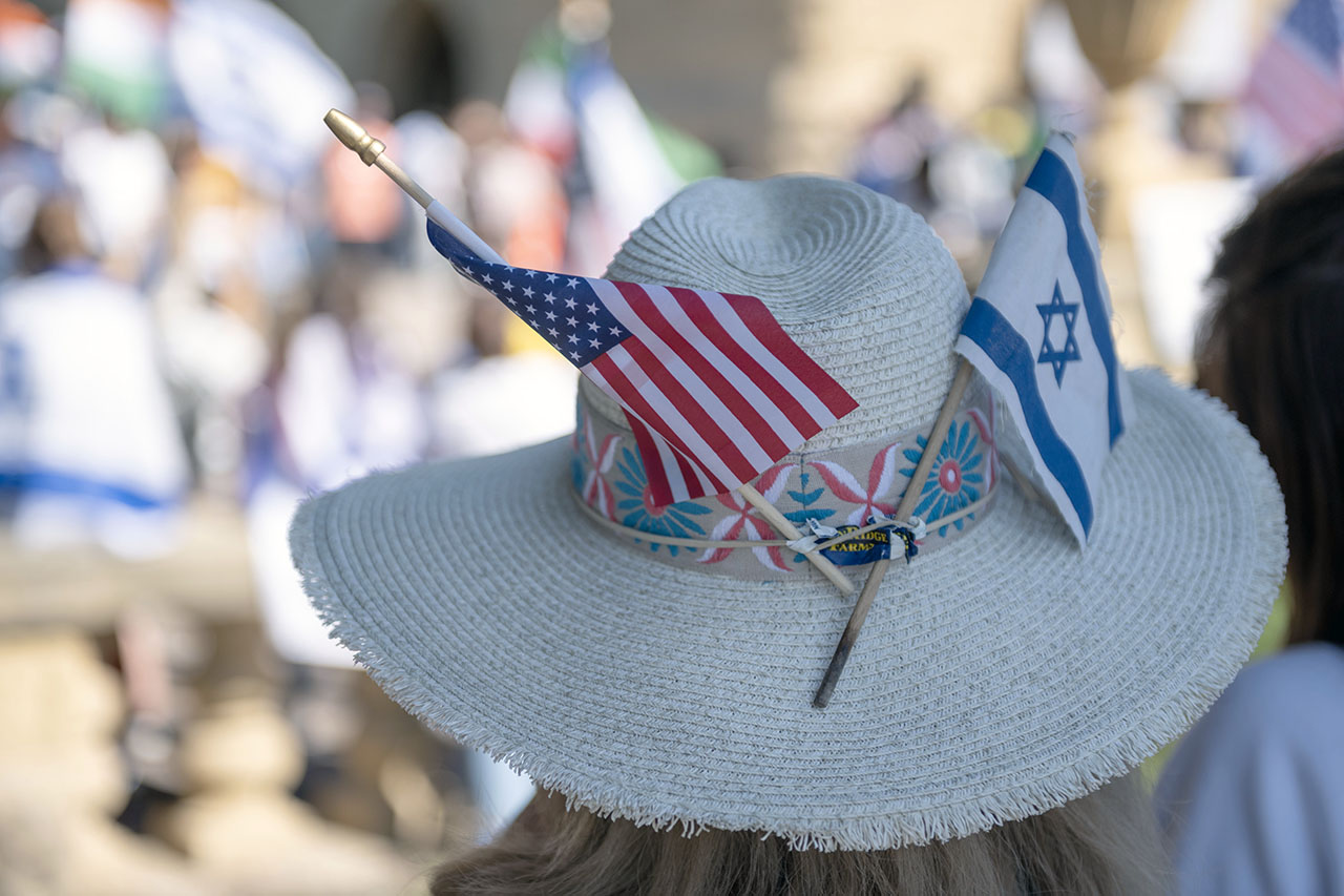 a woman seen from behind wearing a sunhat with small american and israeli flags sticking up from the hatband
